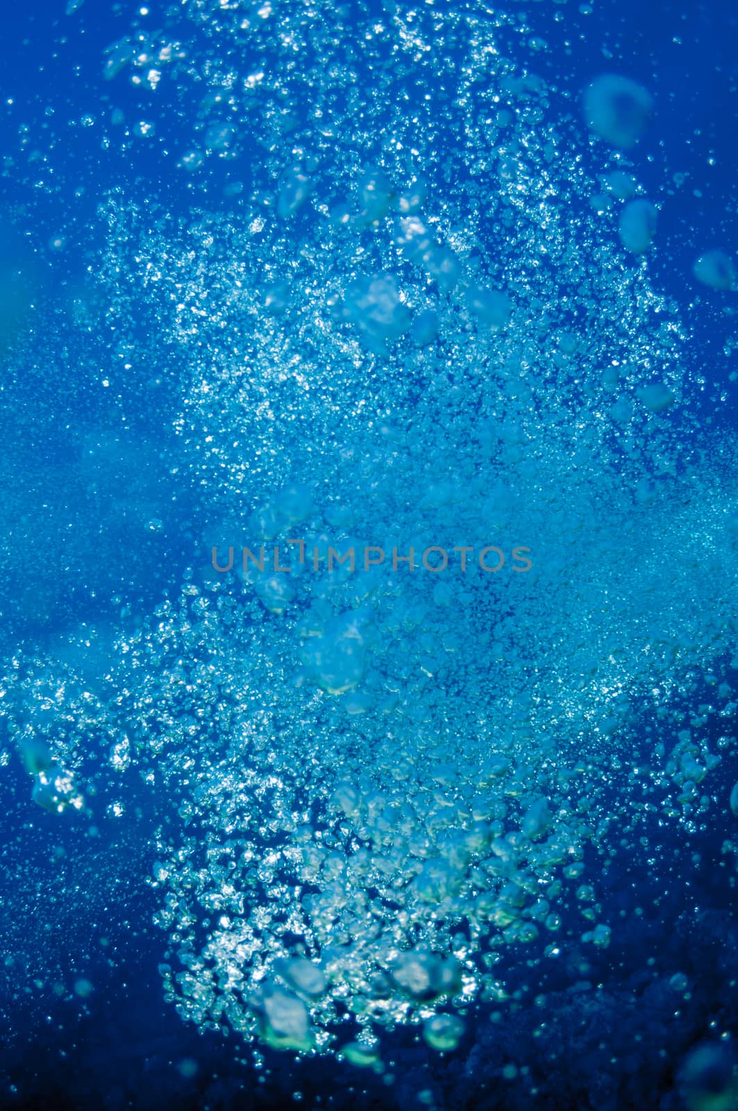 The picture shows underwater bubbles which raise from the depth of blue sea