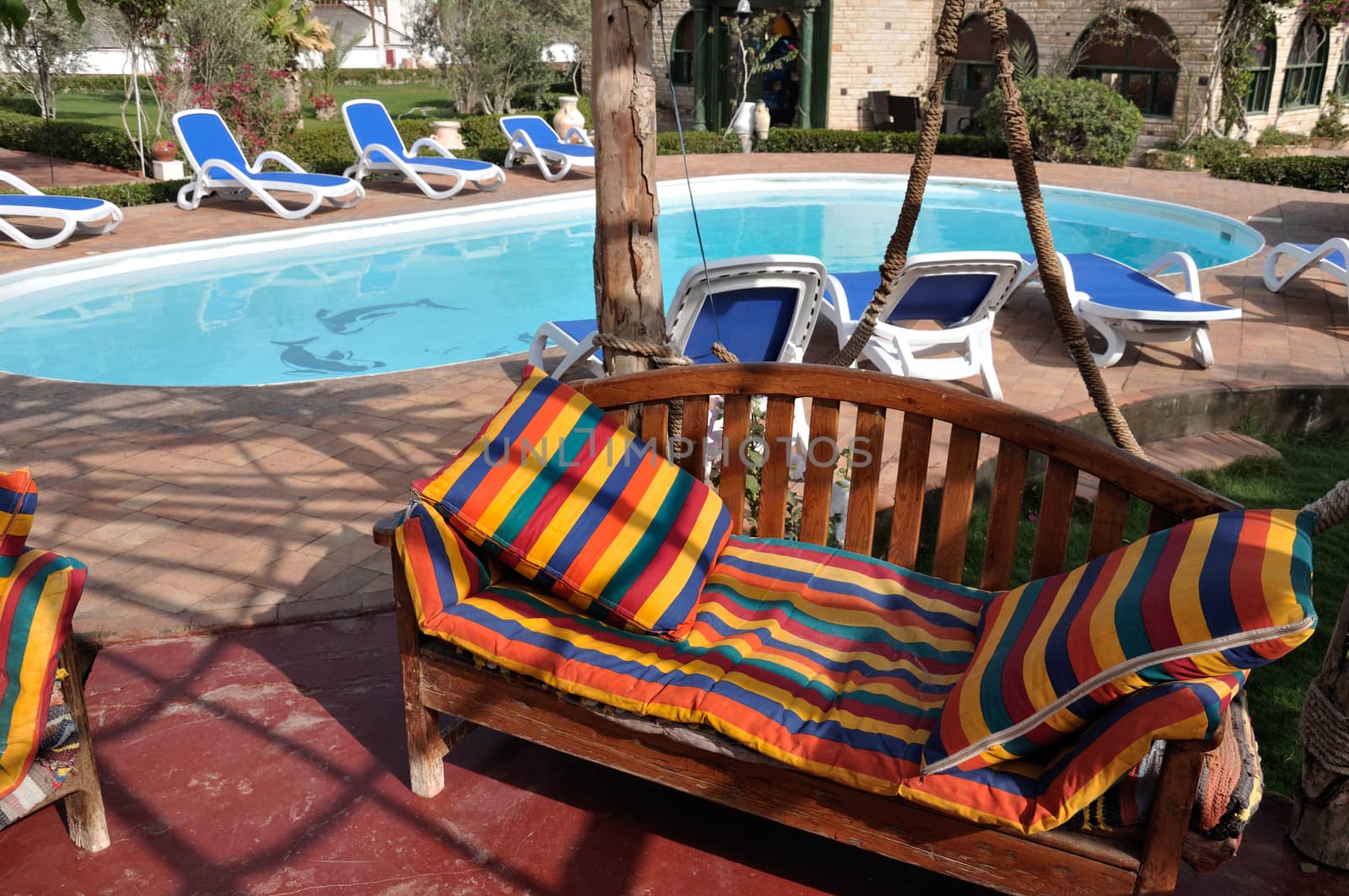 Relaxing picture of the cold hotel swimming pool with clear water and some chairs, trees and lounges around