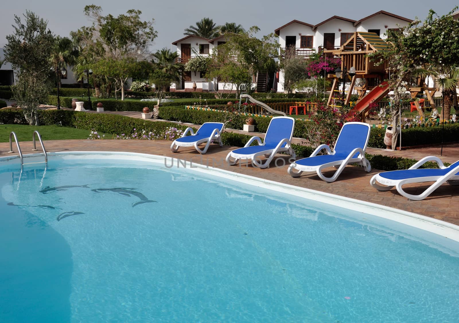 Relaxing picture of the cold hotel swimming pool with clear water and some chairs, trees and lounges around