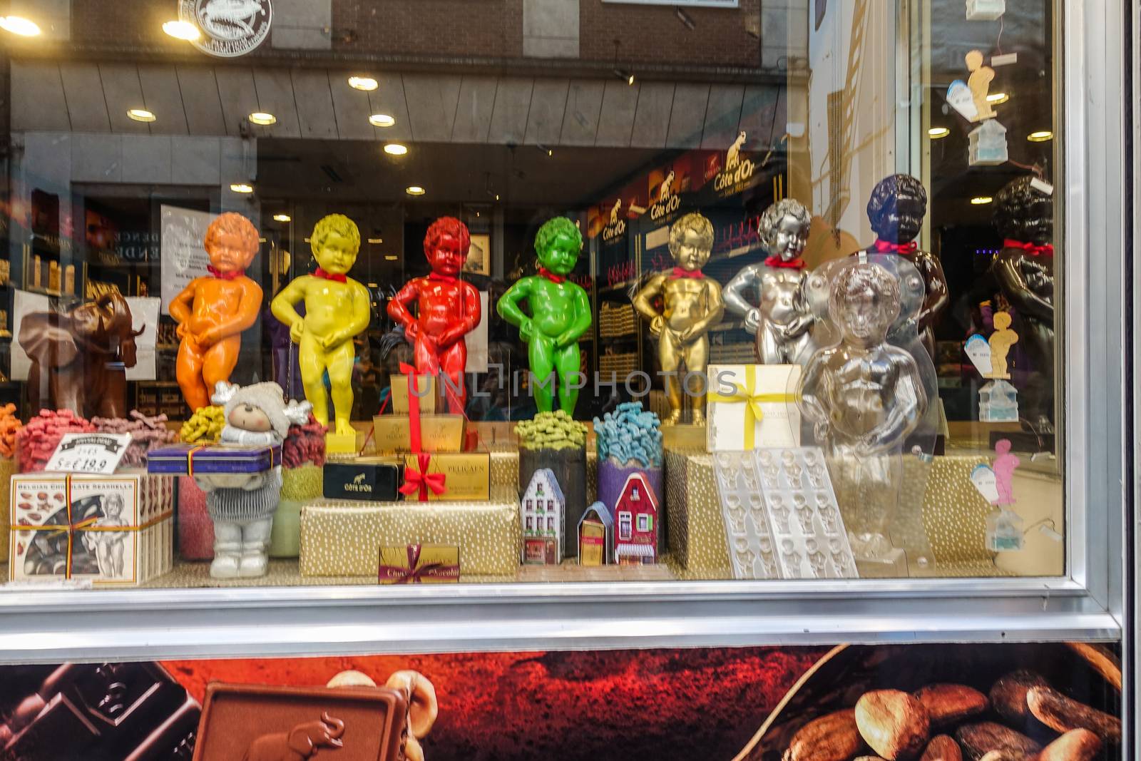 Brussels, Belgium - June 22, 2019: Large chocolate Manneken Pis statues in different colors posing on top of collection of chocolat gifts in window of confectionery store.