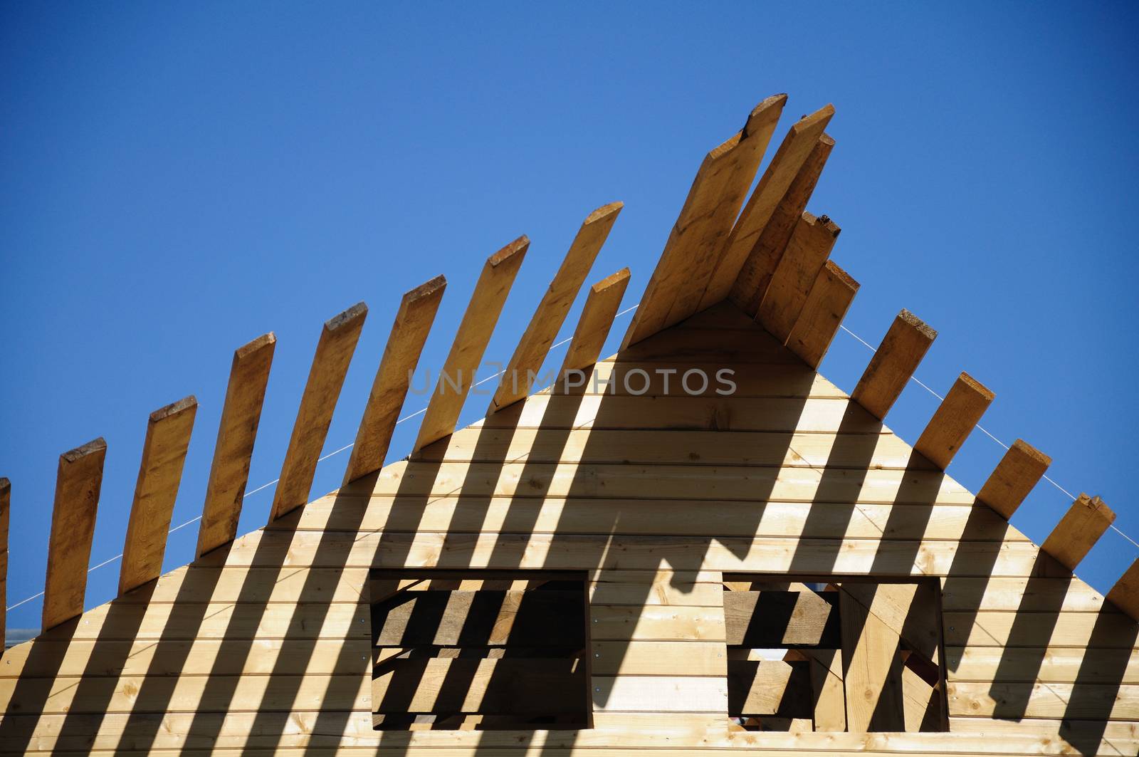 The unfinished wooden roof and empty windows at the blue sky background, up front view