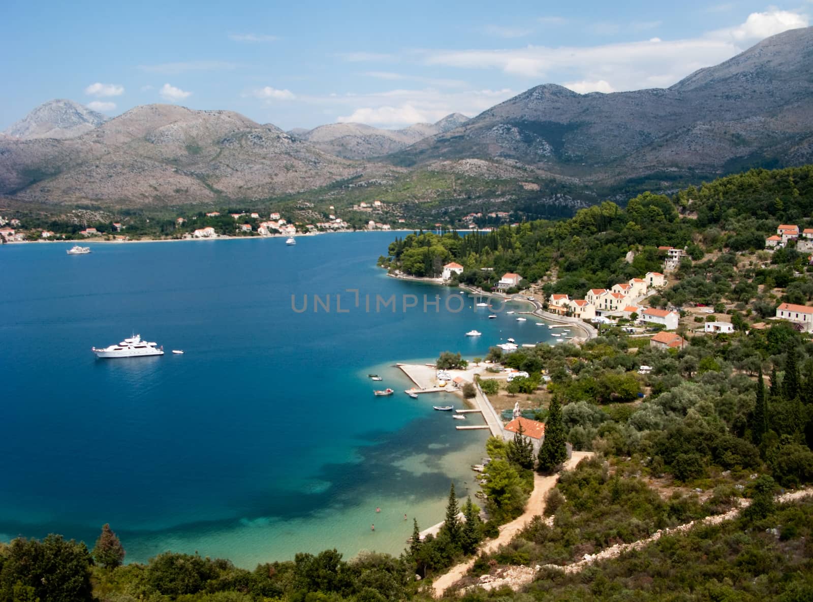 This is a beatiful picture of the mediterranean sea gulf, surrounded by mountains, with attractive yacht in the middle.