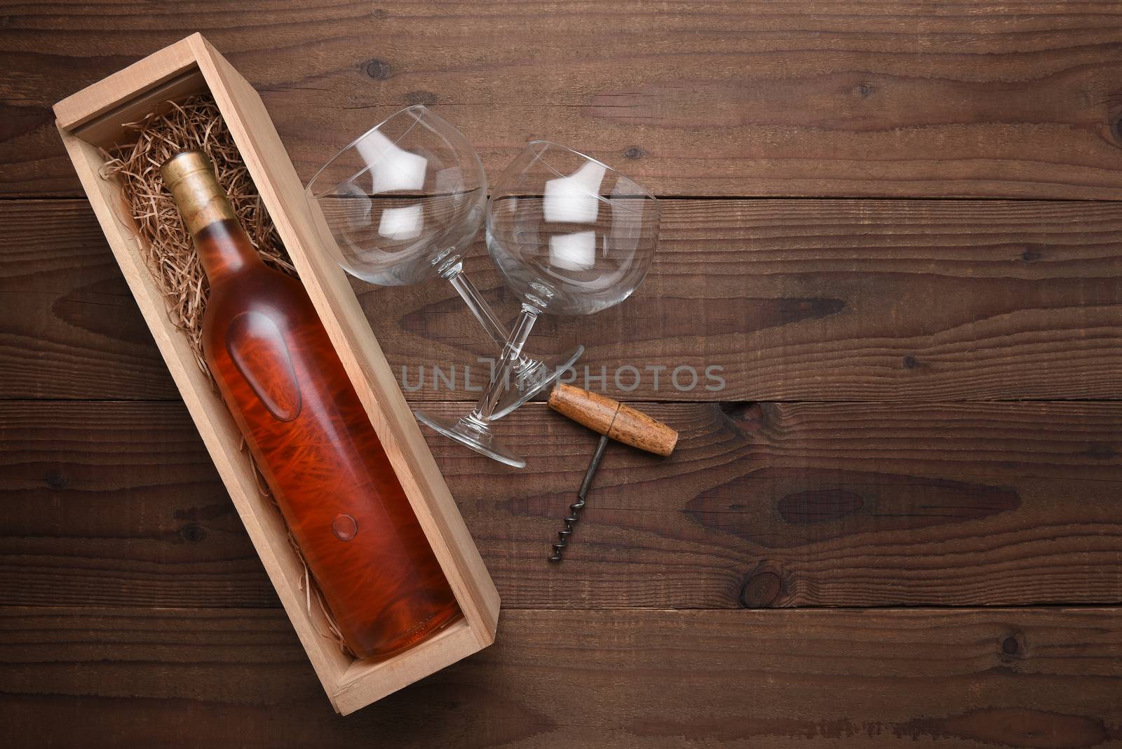 High angle flat lay still life of a blush wine bottle in a wood box with two wine glasses and corkscrew. Horizontal format on rustic wood table with copy space.