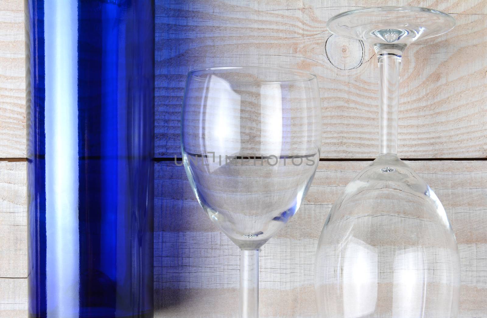 High angle shot of a blue wine bottle and two wine glasses on a rustic white wood table. Horizontal format.