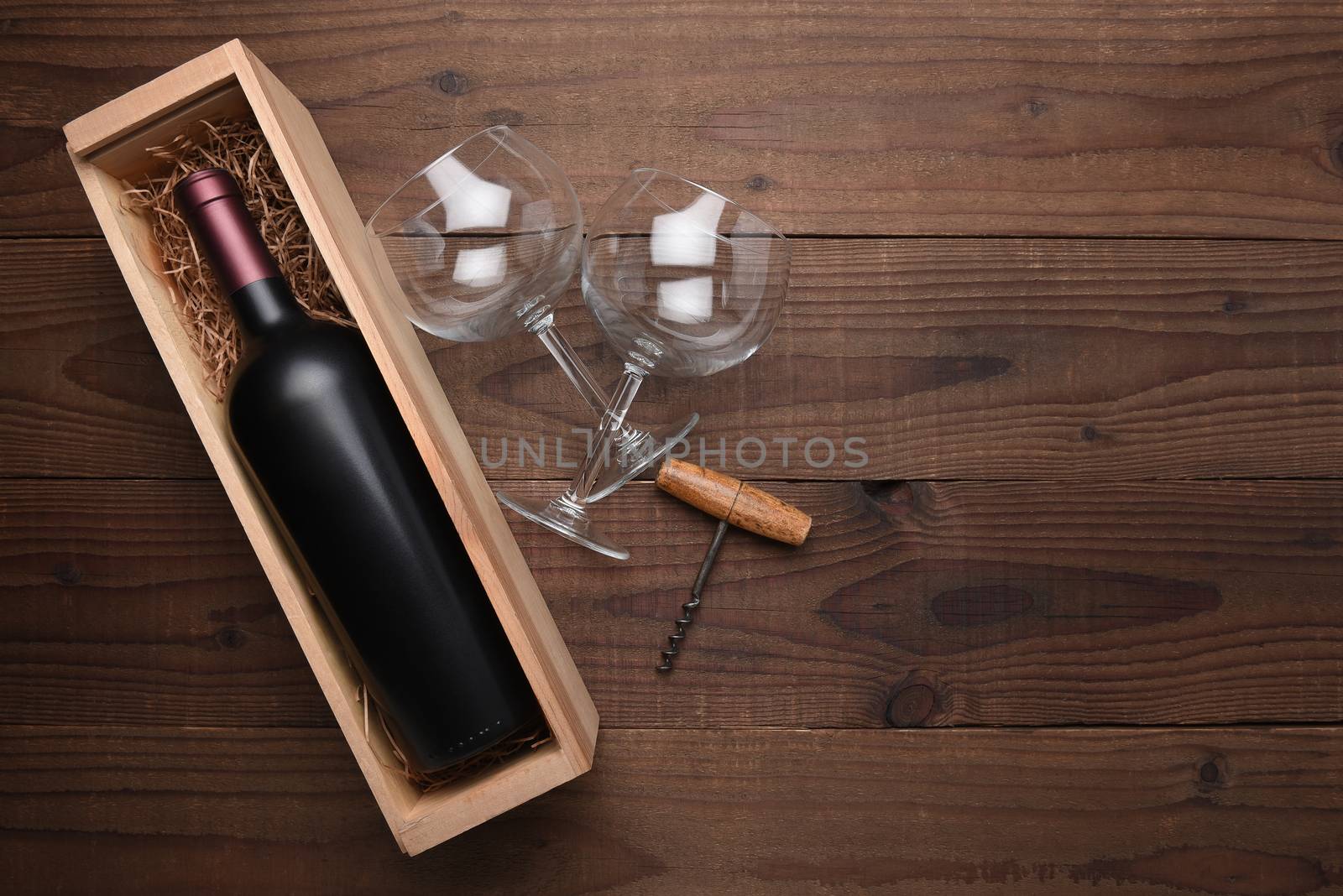 High angle flat lay still life of a wine bottle in a wood box with two wine glasses and corkscrew. Horizontal format on rustic wood table with copy space.