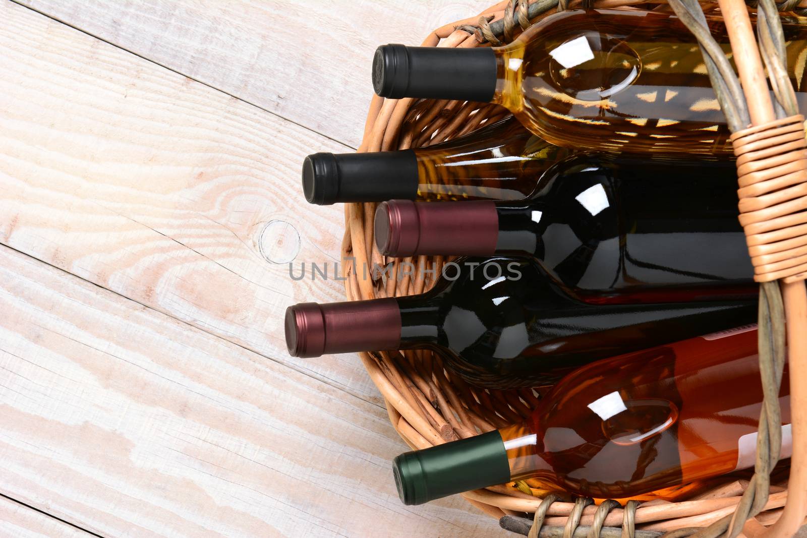 A high angle shot of wine bottles in a basket on a whitewashed wood farmhouse style kitchen table. Horizontal format with copy space.