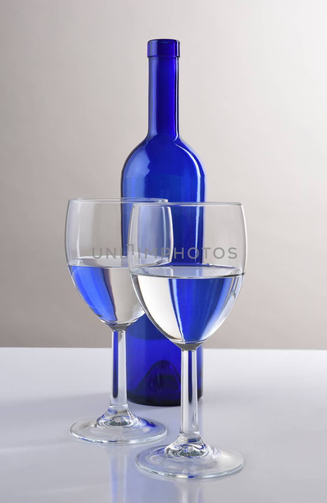 A blue wine bottle behind two half filled glasses with the bottles reflection.