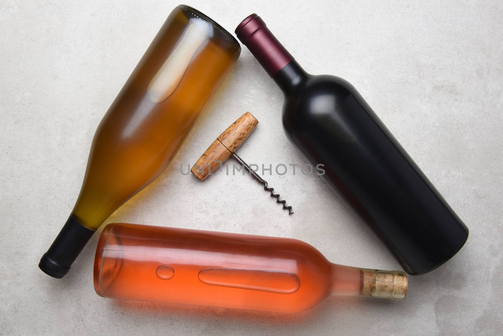 Cabernet, Rose, Chardonnay: Overhead view of a group of three different bottles arranged in a triangle with a corkcscrew in the middle.