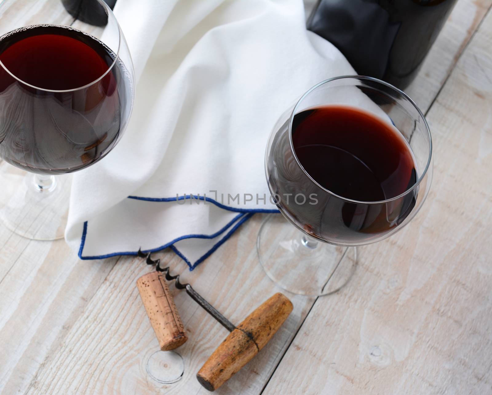 Two wineglasses of red wine on a wood table with antique cork screw. Horizontal format shot from a high angle.