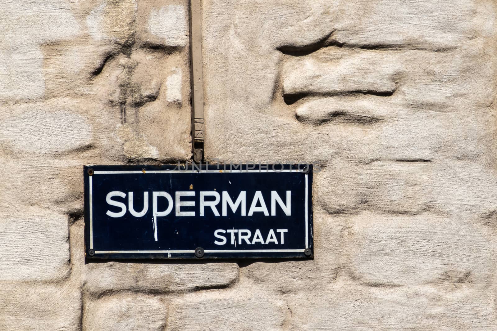 Antwerpen, Belgium - June 23, 2019: Closeup of white on blue street name sign of Suderman Straat converted into Superman Straat. Beige wall background.