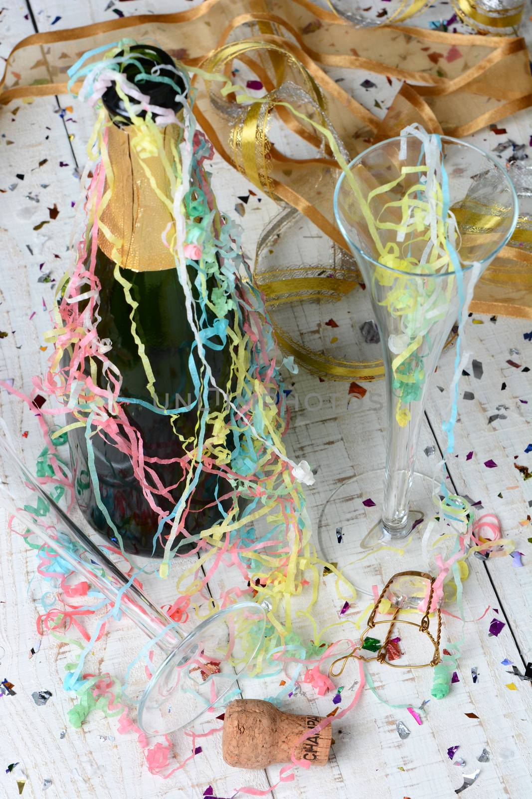 High angle shot of a Champagne bottle, streamers and confetti after a New Years Eve Party. Vertical format with shallow depth of field. Focus is on the foreground and table top.