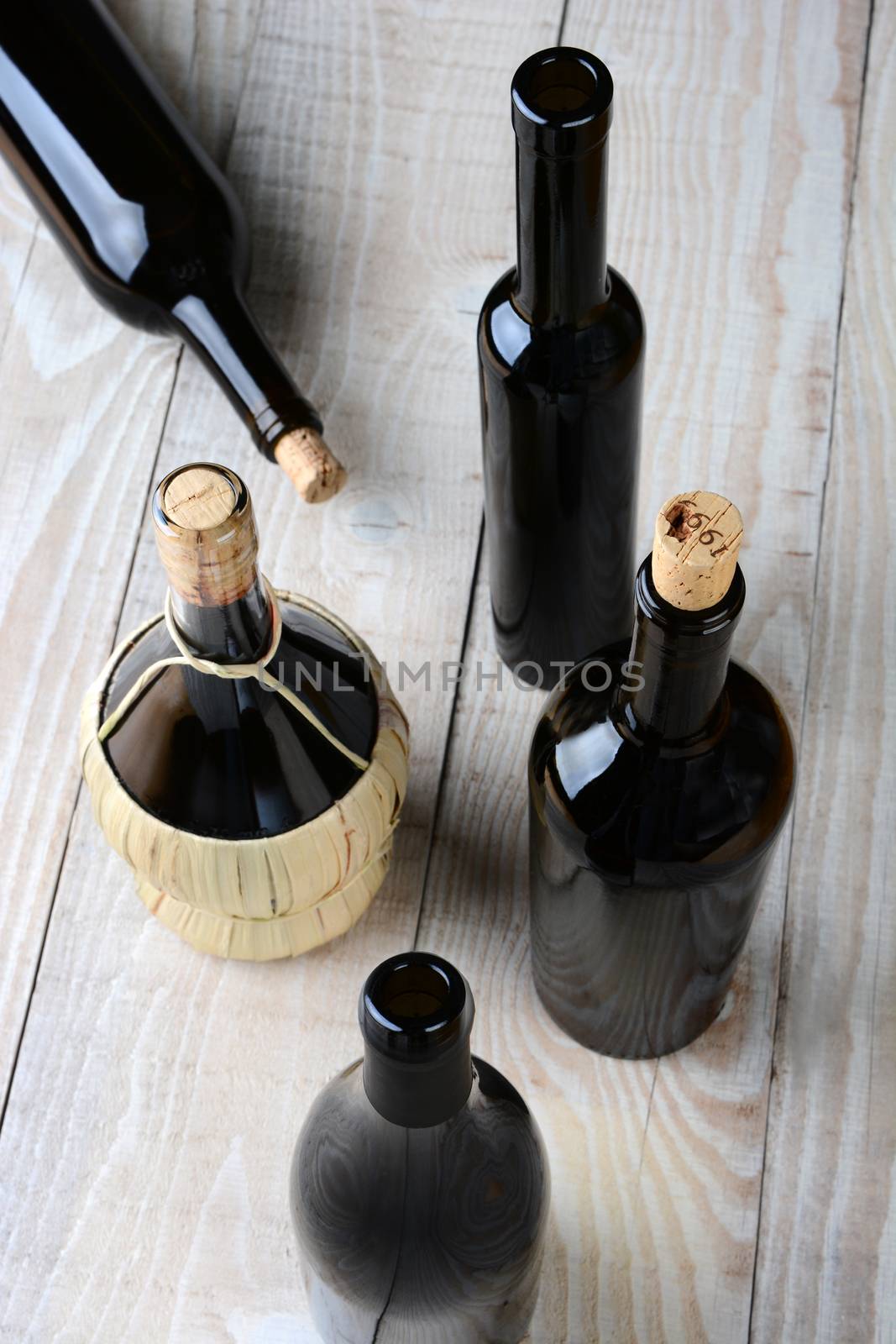 High angle shot of assorted wine bottles on a white rustic wood table. Shallow depth of field with focus on the tops. 