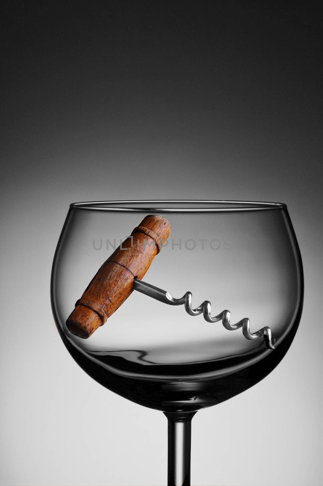 An antique cork screw in a wine glass against a light to dark gray background.