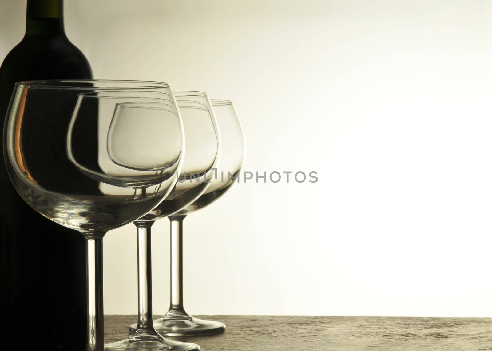 A row of Empty Wine Glasses with red wine bottle in silhouette behind horizontal format with warm light