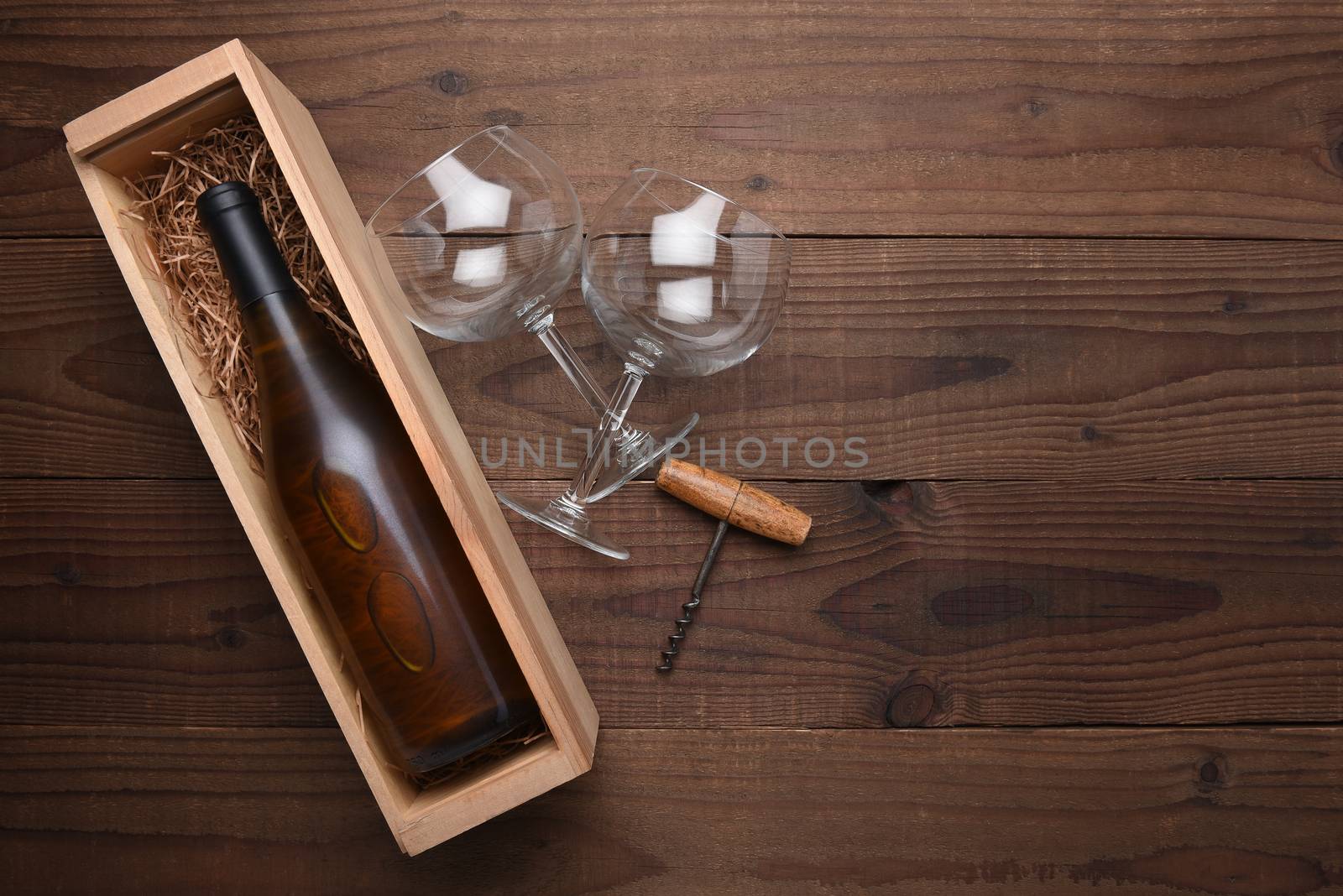 High angle flat lay still life of a Chardonnay wine bottle in a wood box with two wine glasses and corkscrew. Horizontal format on rustic wood table with copy space.