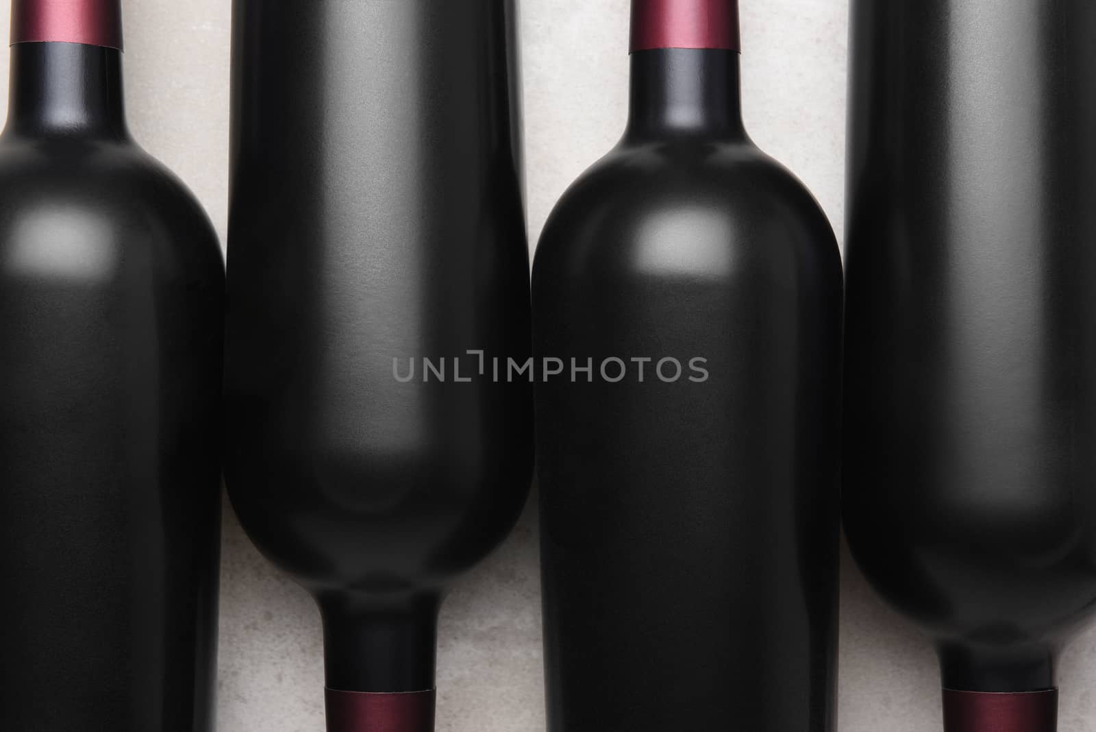 Cabernet Wine Bottles: Closeup overhead shot of four red wine bottles in alternating orientation on concrete table top.