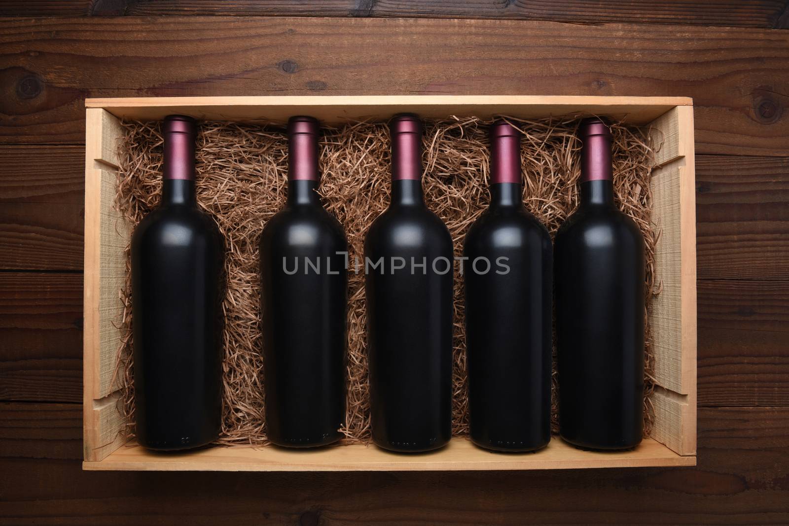 Case of Red Wine: Top view of a wood case of red wine bottles on a dark wood table, the case is filled with packing straw.