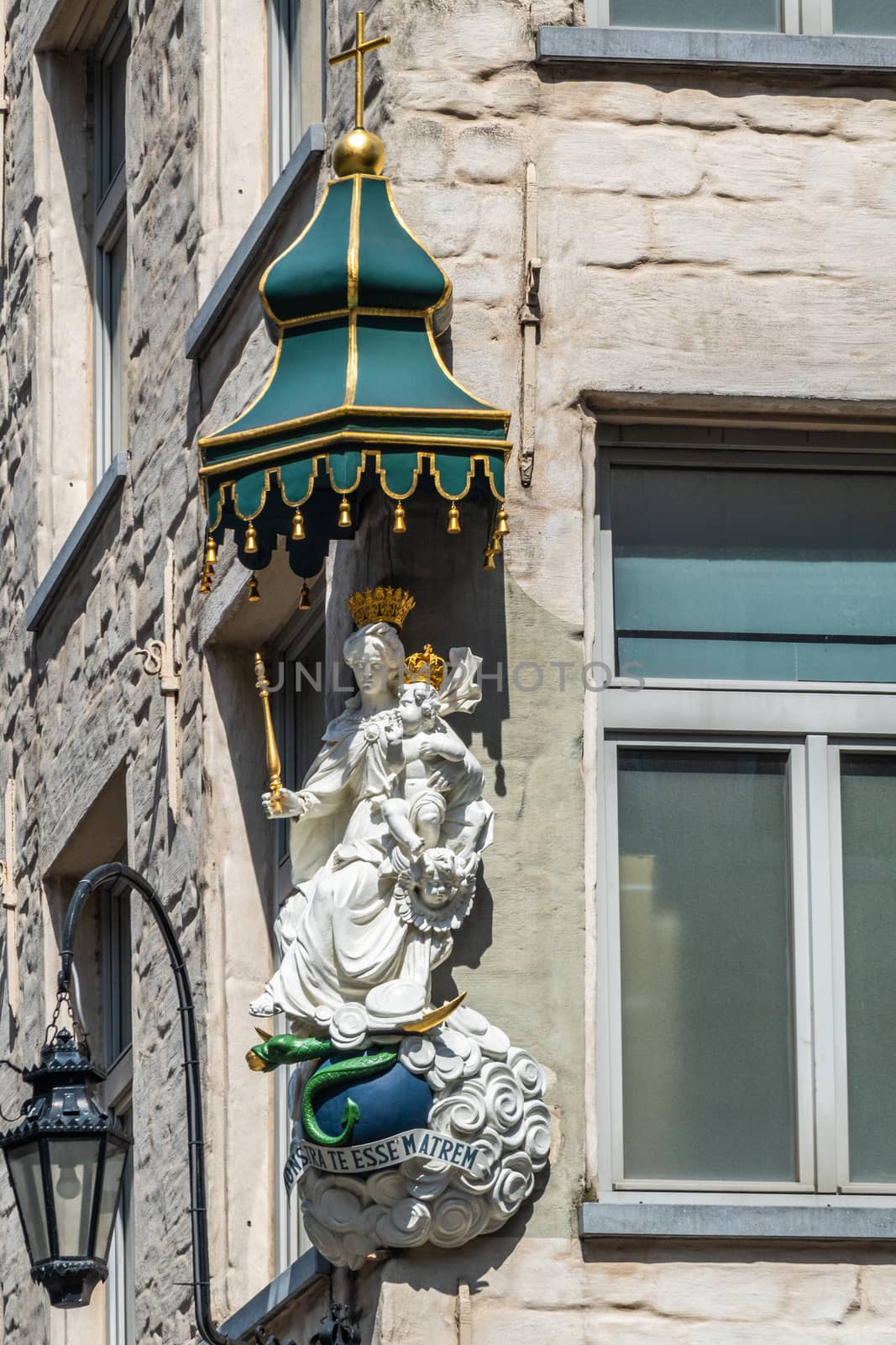 Antwerpen, Belgium - June 23, 2019: Closeup of white stone with golden crowns statue of Madonna with child on corner of Eiermarkt and Suderman Straat. Gray facade with window and streetlantern.