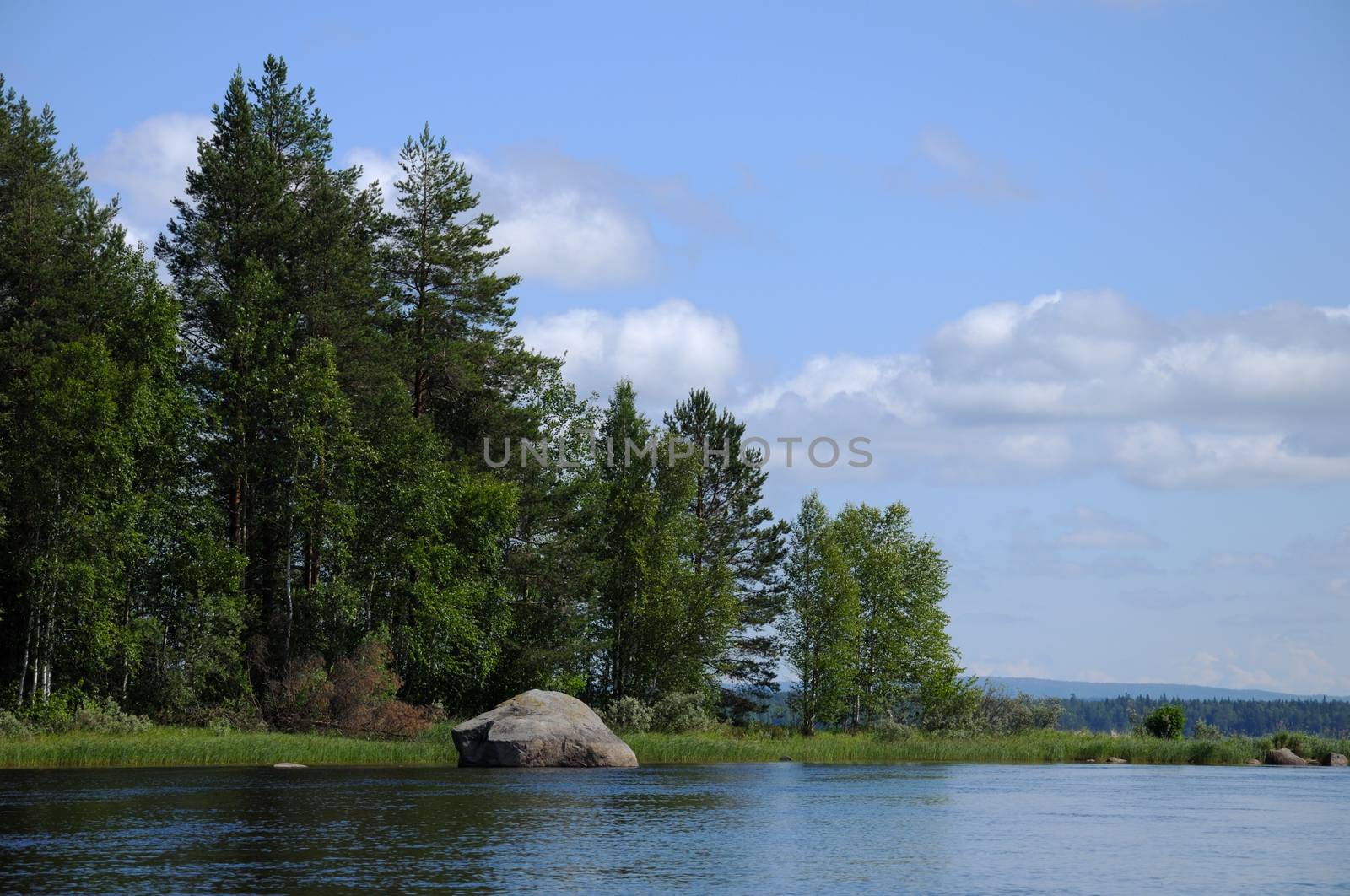 The beautiful picture of Karelian forest at the edge of a lake, and some huge boulder in this lake