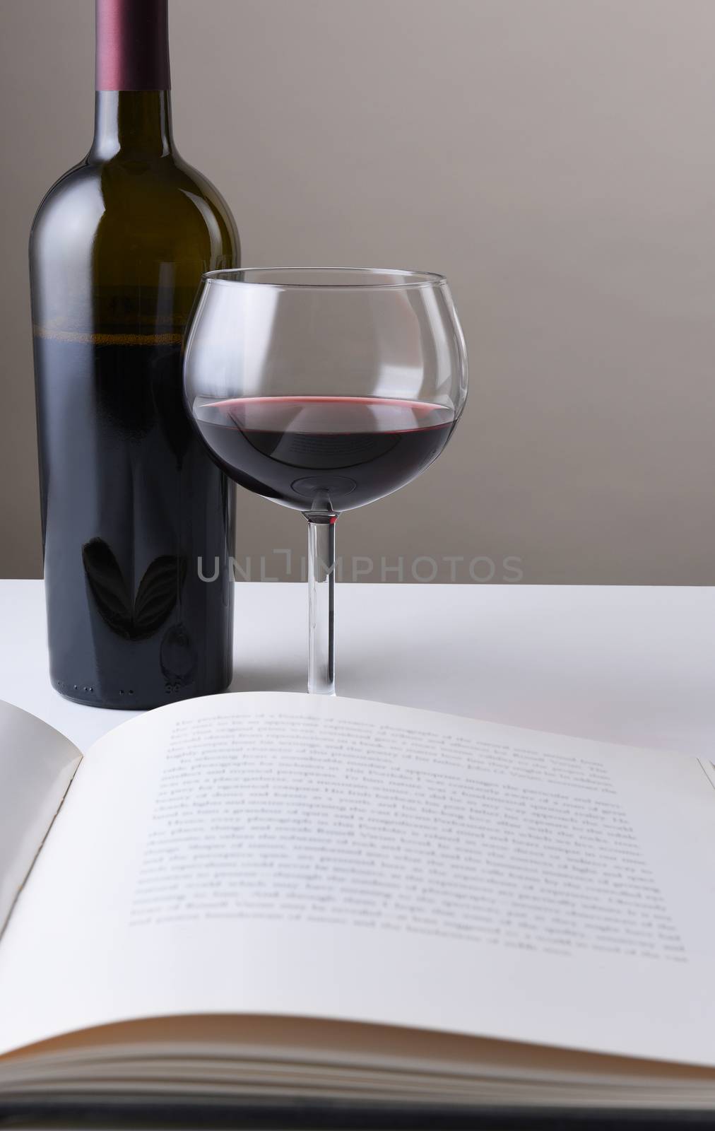 Wine bottle and glass behind an open book. The pages of the book are blurred. Vertical format with copy space.
