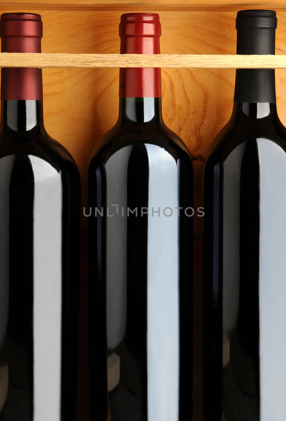 Closeup of three red wine bottles in a wooden case. Vertical format.