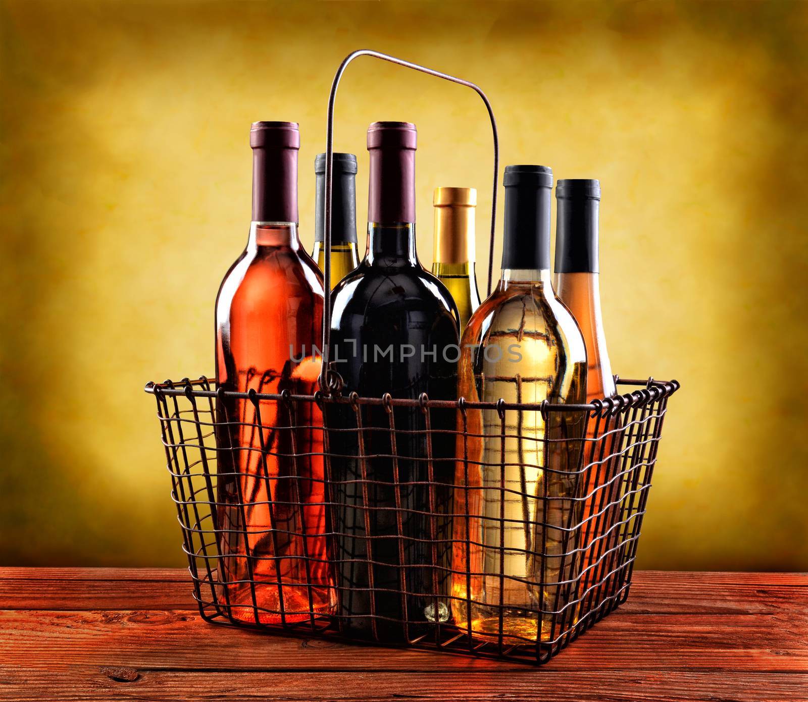 A wire shopping basket filled with wine bottles on a rustic wood table with a mottled background with warm tones.