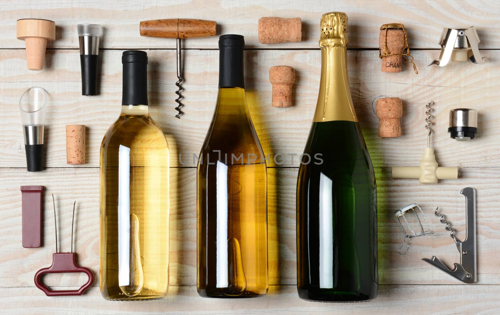 High angle shot of Wine and Champagne bottles surrounded by accessories such as corkscrews, stoppers, pourers and corks. Horizontal format on a rustic white wood table.