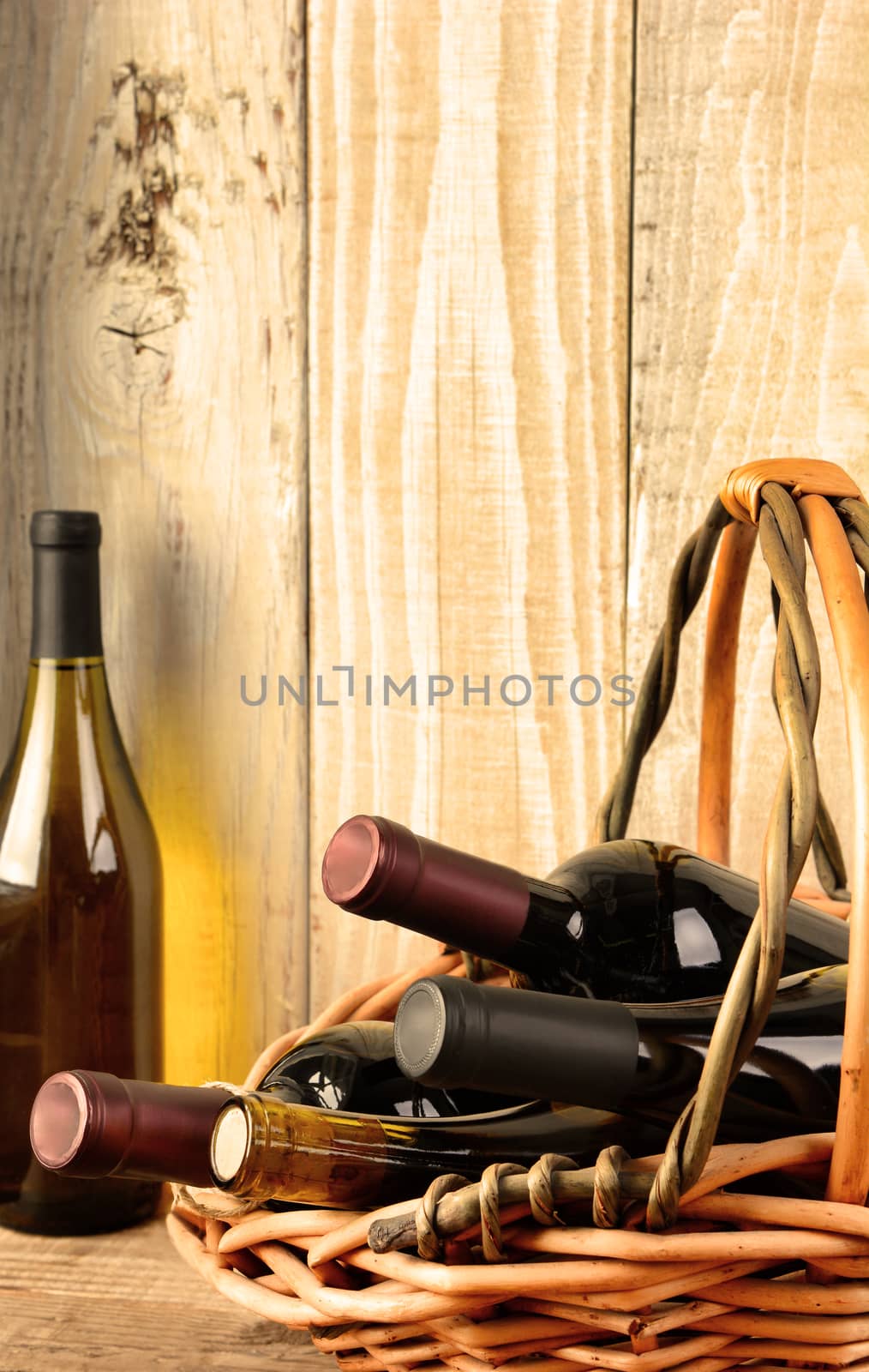 Closeup of a wine still life with warm afternoon window light. A basket with assorted bottles and a chardonnay bottle in the corner against a rustic wood background. Bottles have no labels.