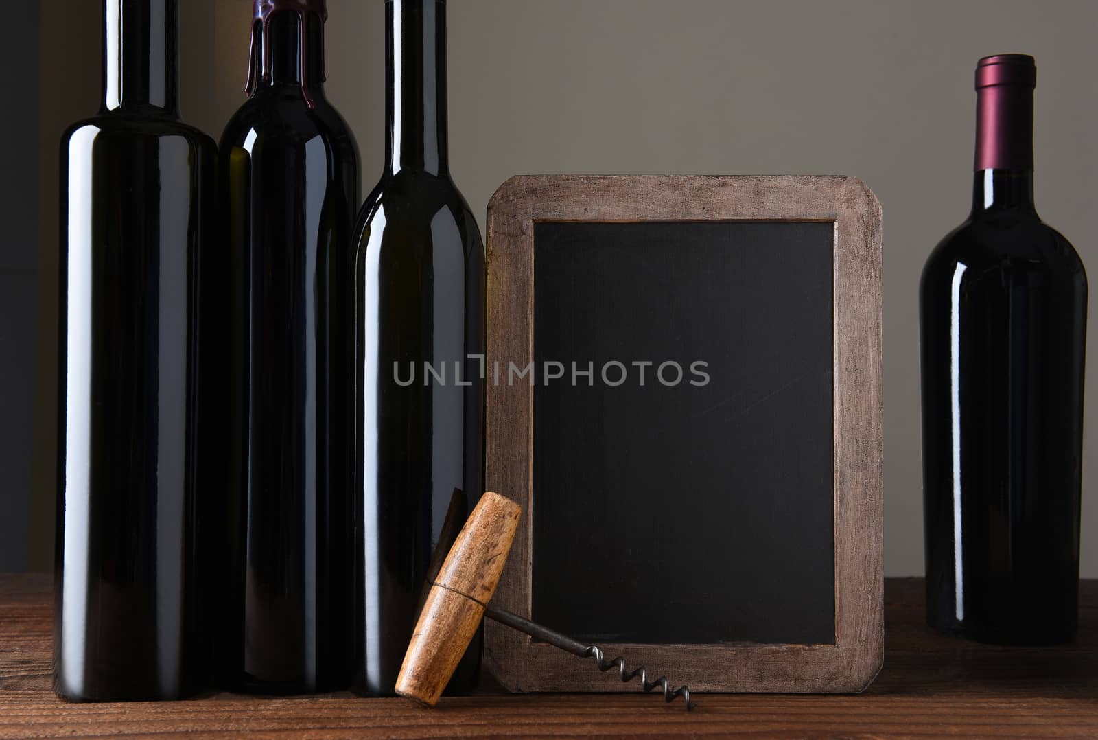 A wine menu chalk board with bottles of wine and cork screw. On a rustic wood table with light to dark grey background.