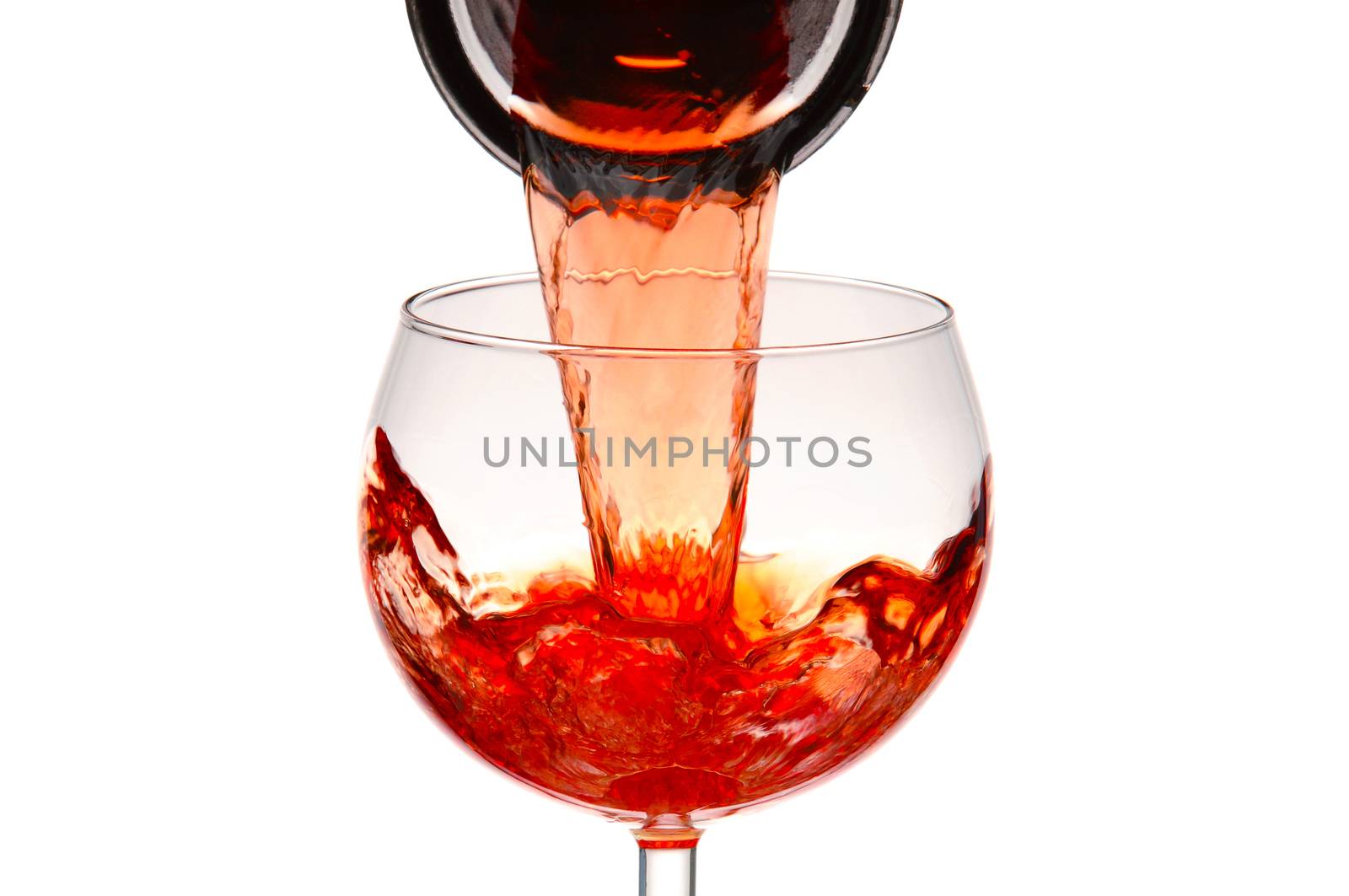 Closeup of a wineglass with red wine pouring from a carafe.