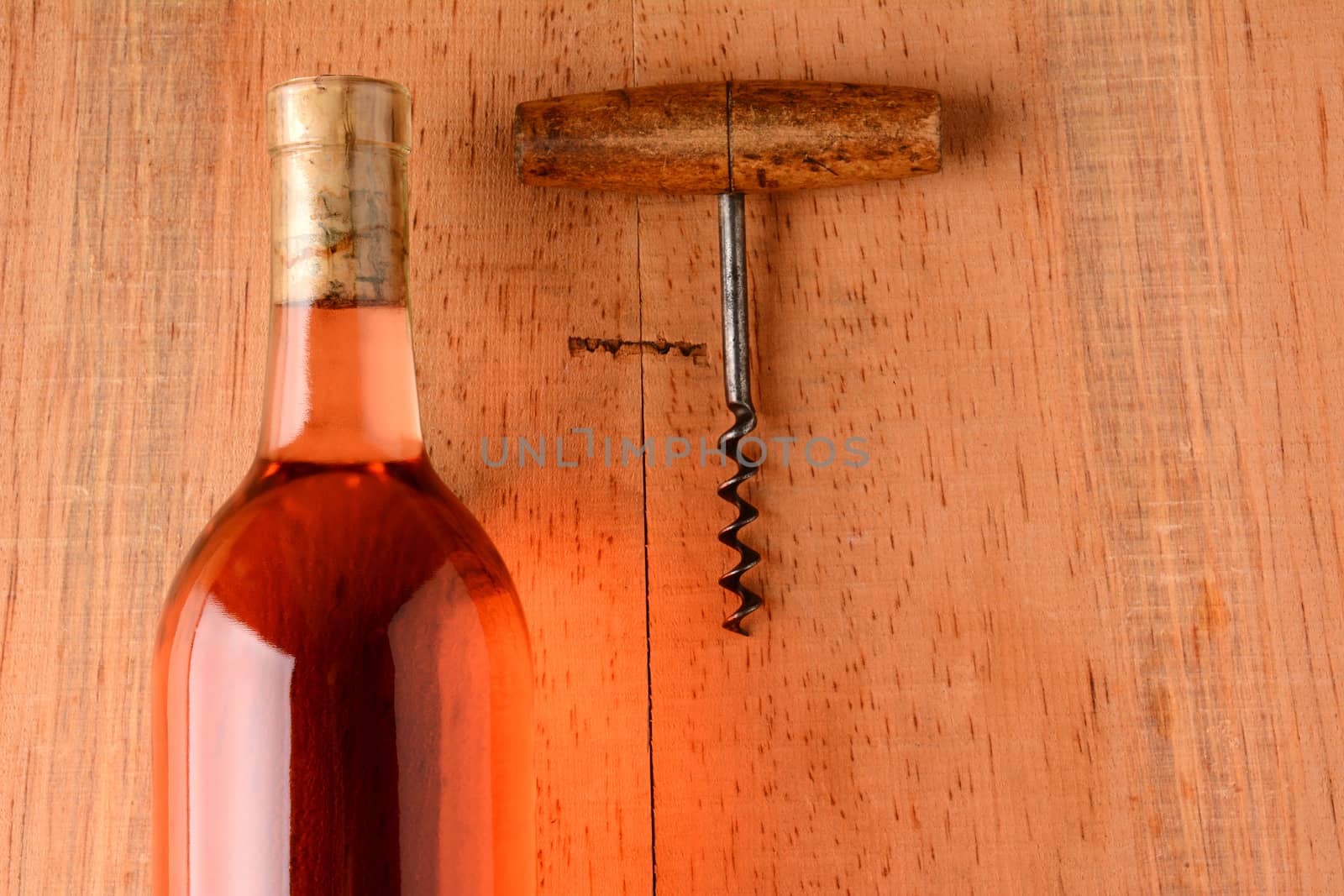 A blush wine bottle and corkscrew on a rustic wood surface with strong side light. Closeup in horizontal format with copy space.
