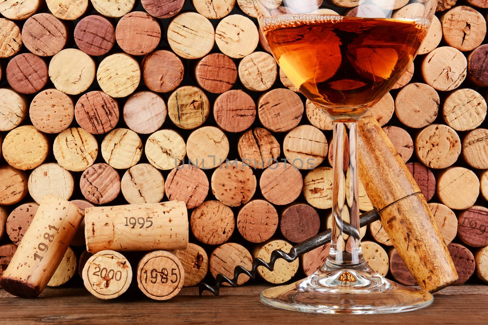 Closeup of a wineglass in front of a wall of used corks. An antique cork screw and dated corks are adjacent to the glass. Horizontal format filling the frame.