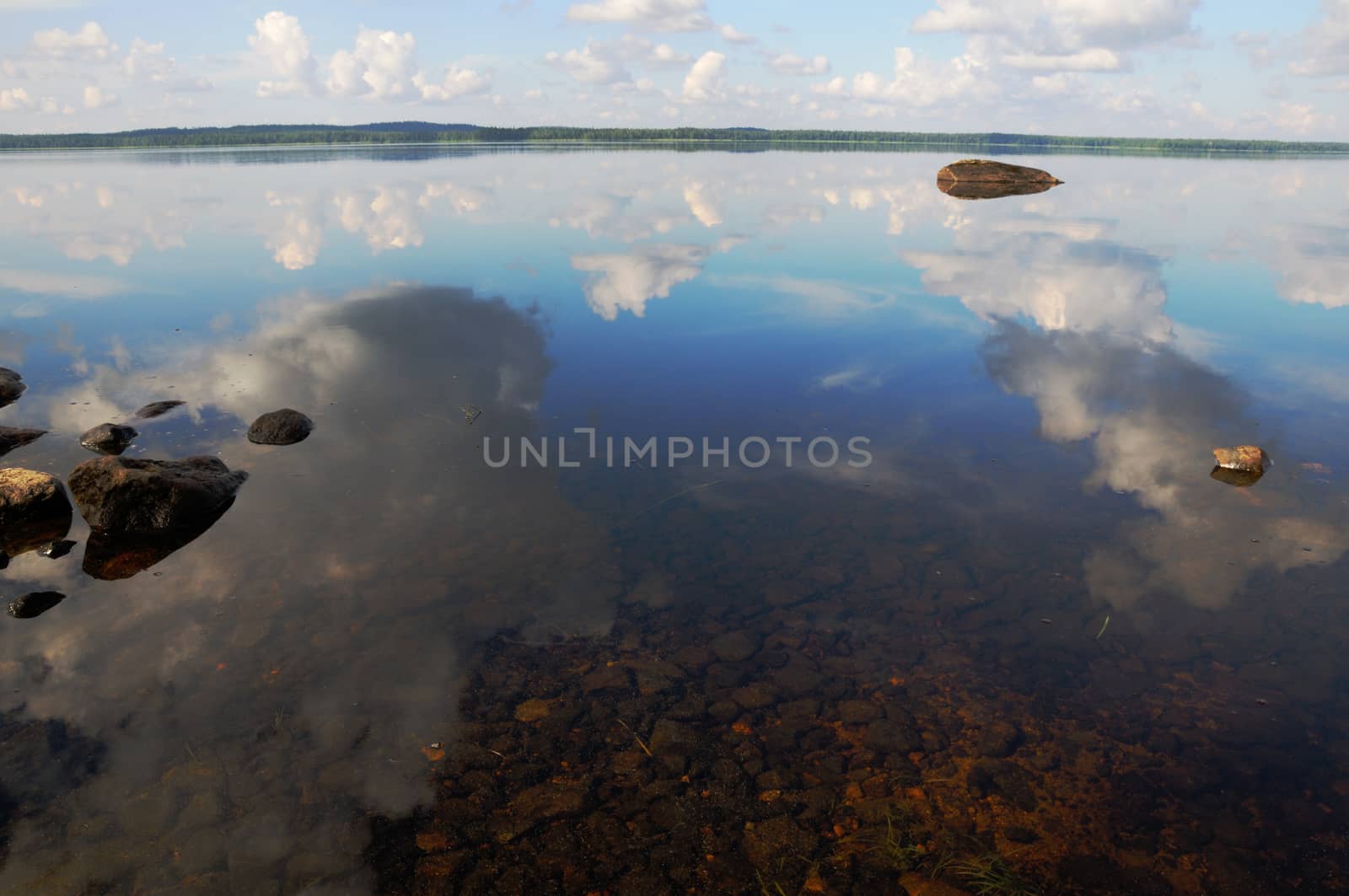 The bottom of the lake with a lot of stones and reflected sky