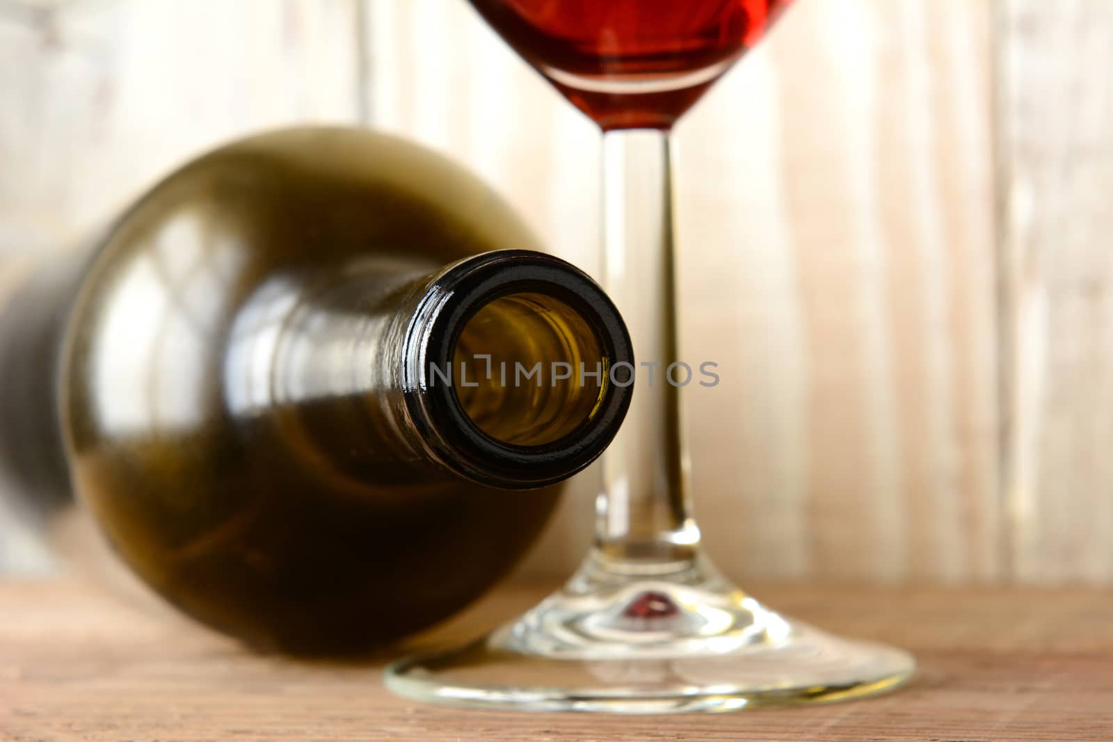 Wine still life with a bottle on its side and the bottom of a glass of red wine on a wood background. Horizontal format with shallow depth of field. 