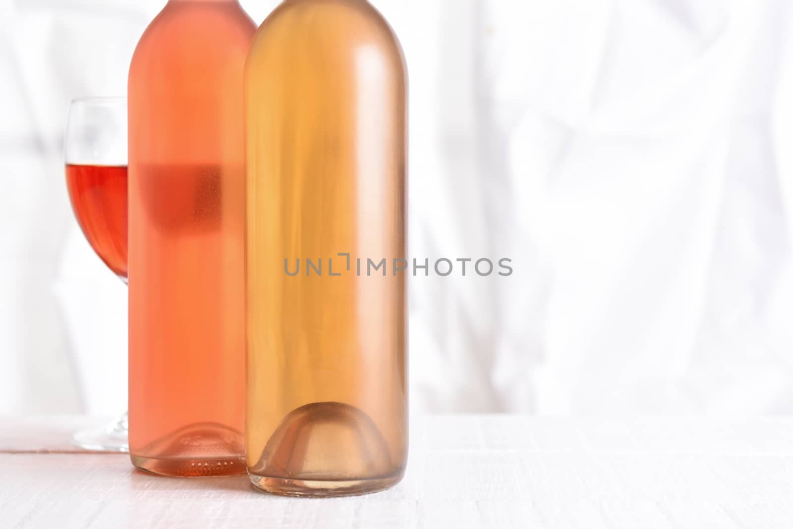 Wine Still Life: High key wine bottles on a white wood table in front of a window.