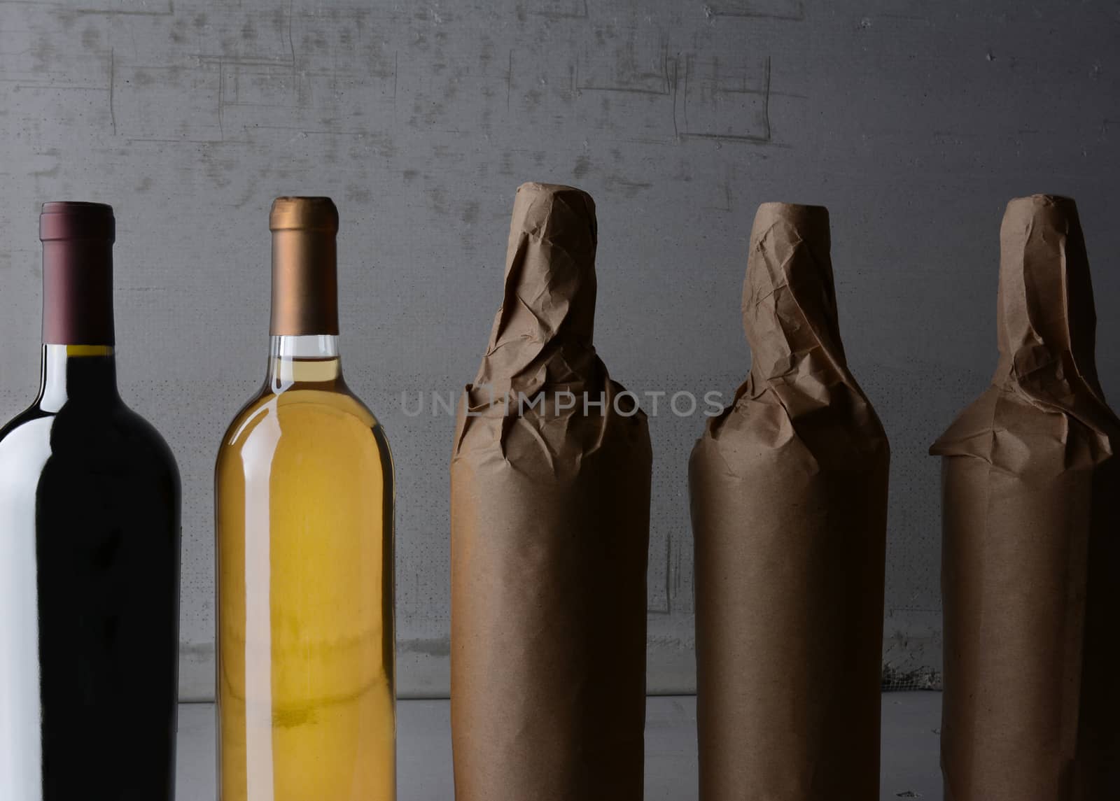 Five Wine Bottles, three wrapped in plain paper with one red wine and one white. Strong side light with copy space. 