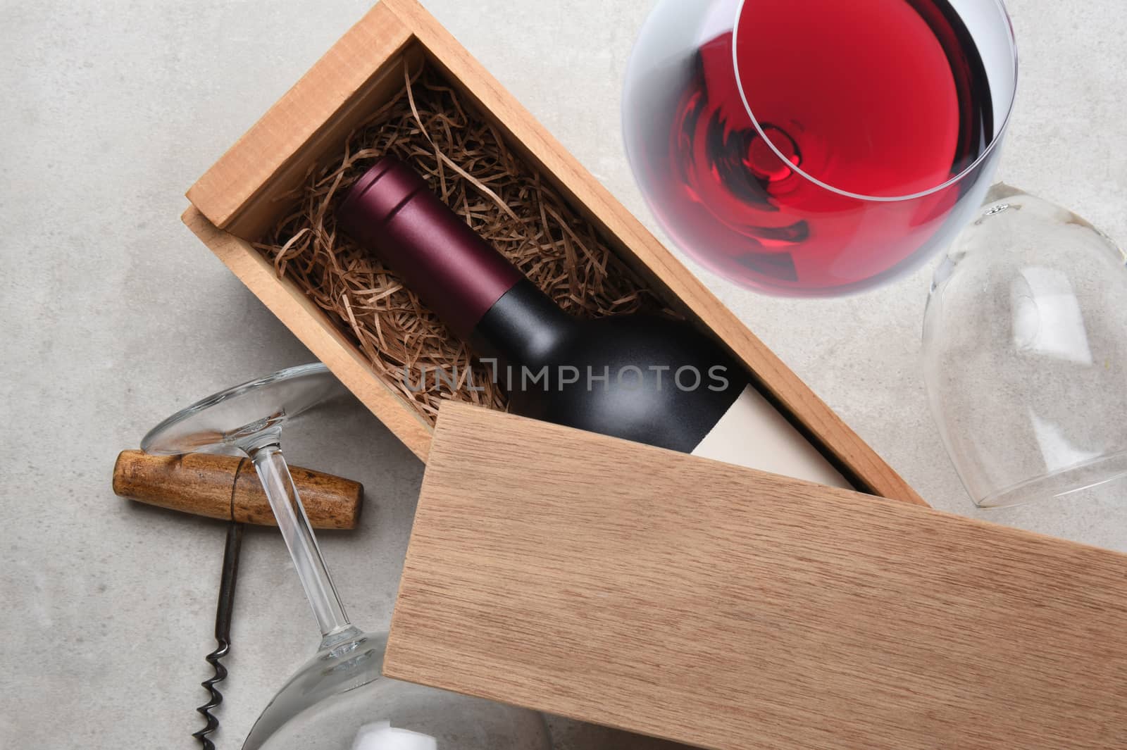 Red Wine Box: A single bottle of Cabernet in a wood box partially covered by its lid with empty glasses and corkscrew with a full glass of red wine .