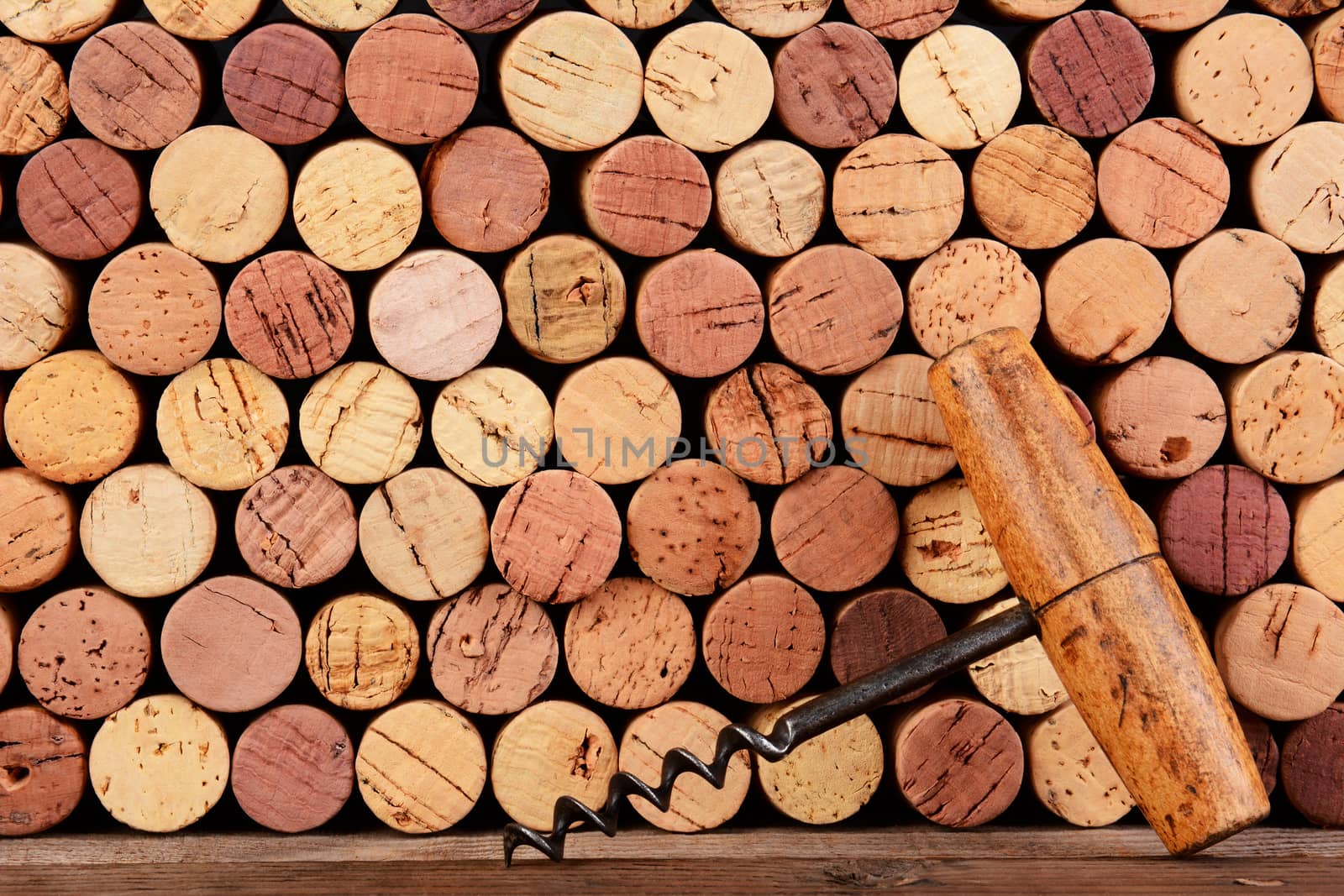 Closeup of an antique cork screw leaning against a wall of use corks. Horizontal format filling the frame.