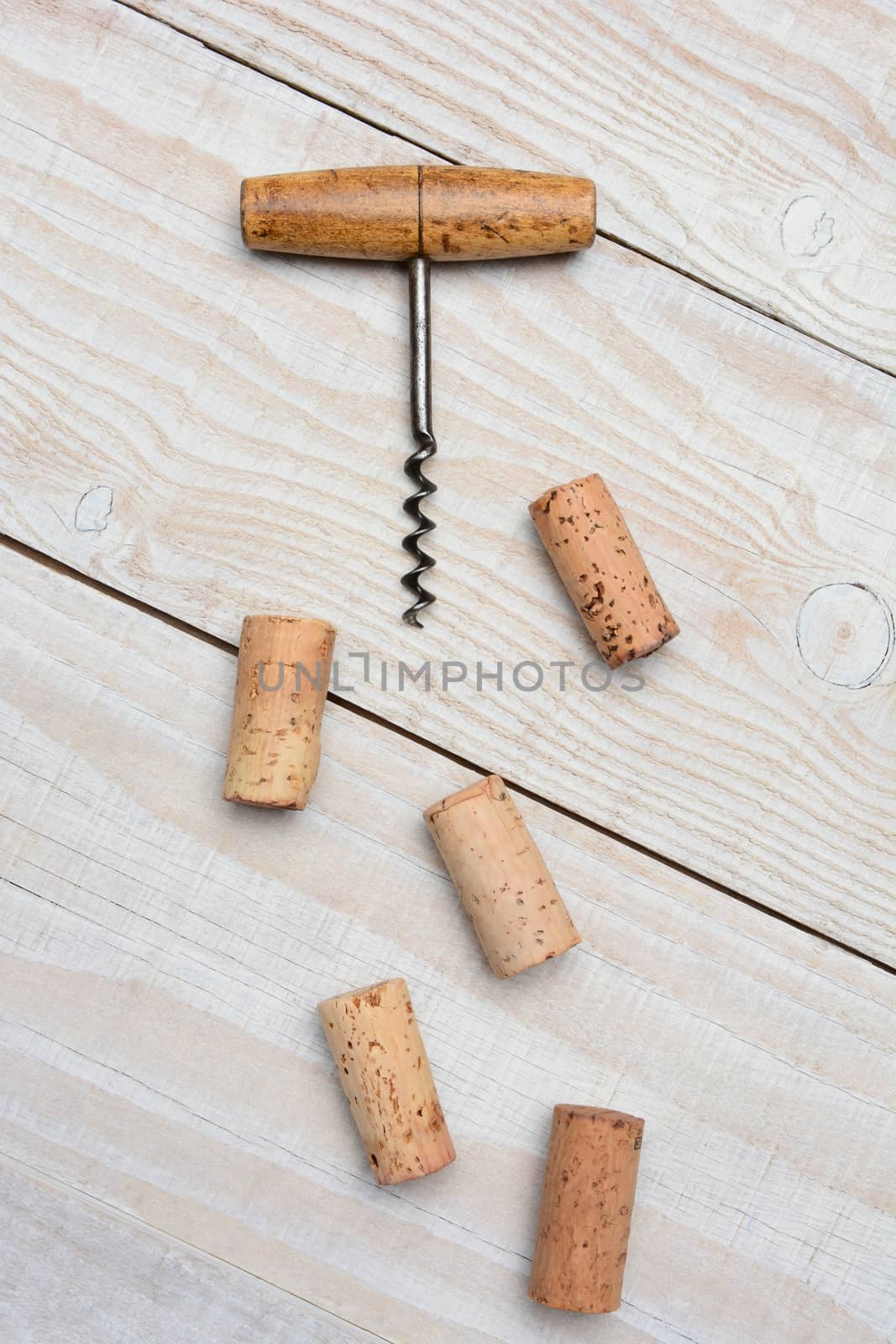 Closeup of an antique cork screw and five used corks on a rustic whitewashed wood table. Vertical format from a high angle.