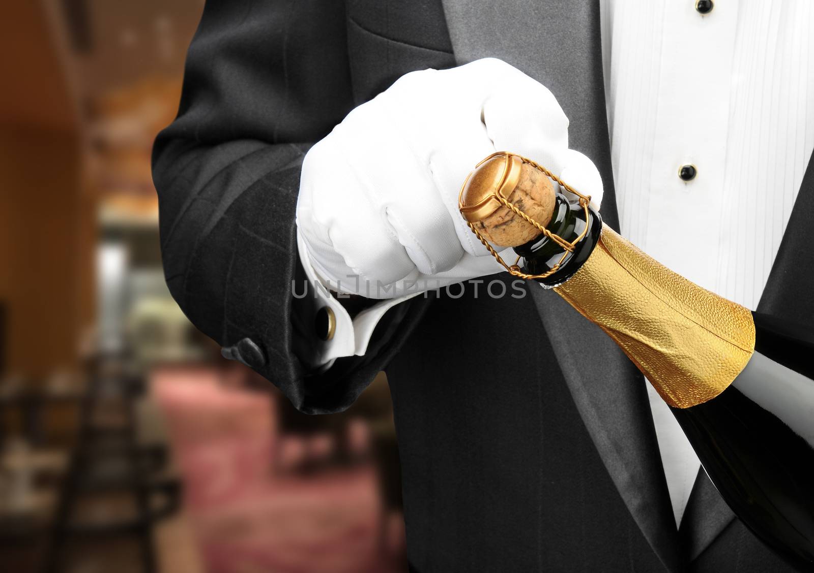 Closeup of a waiter in a restaurant opening a bottle of champagne.