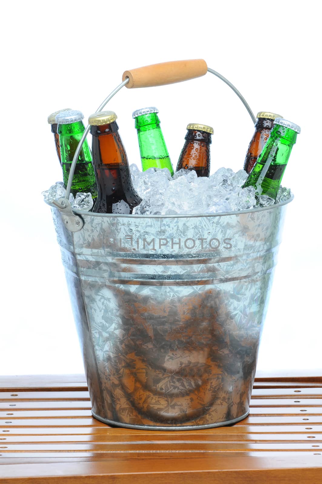 Beer Bucket filled with assorted bottles and ice cubes on teak table in front of a white background.