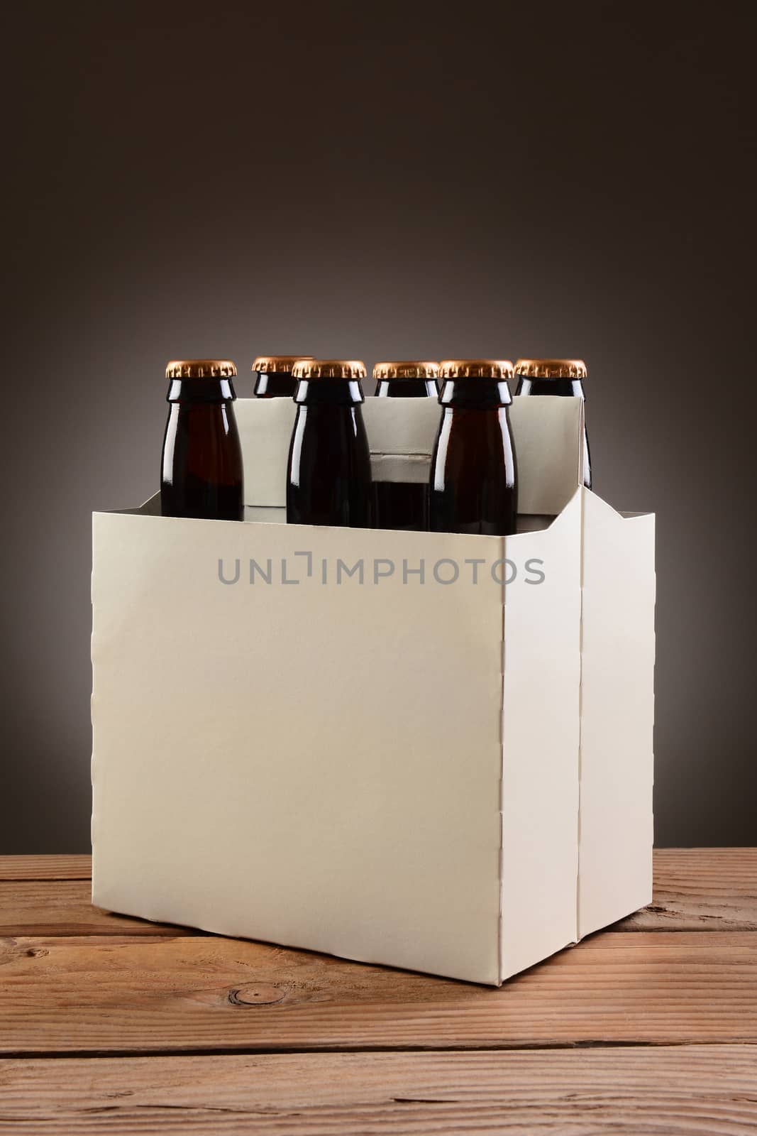 Closeup of a six pack of brown beer bottles on a rustic wooden table. Vertical format with a light to dark gray spot background.