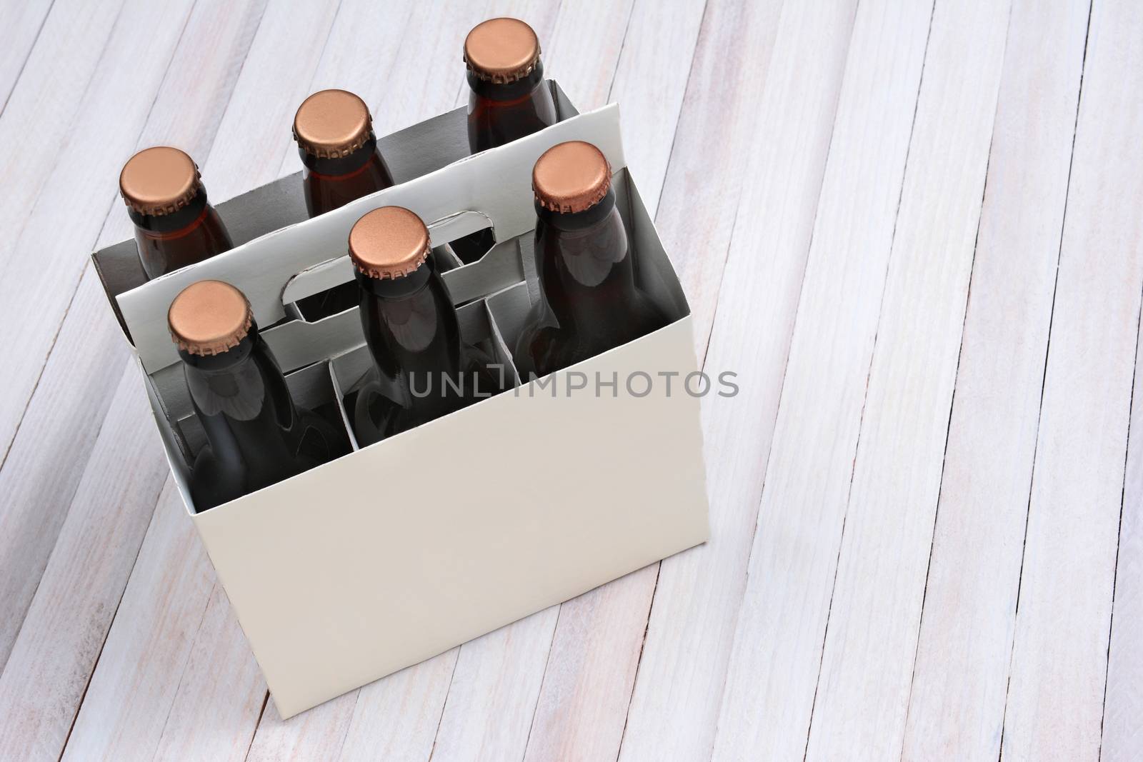 High angle shot of a blank six pack of brown beer bottles on a rustic white wood table. Horizontal format with copy space.