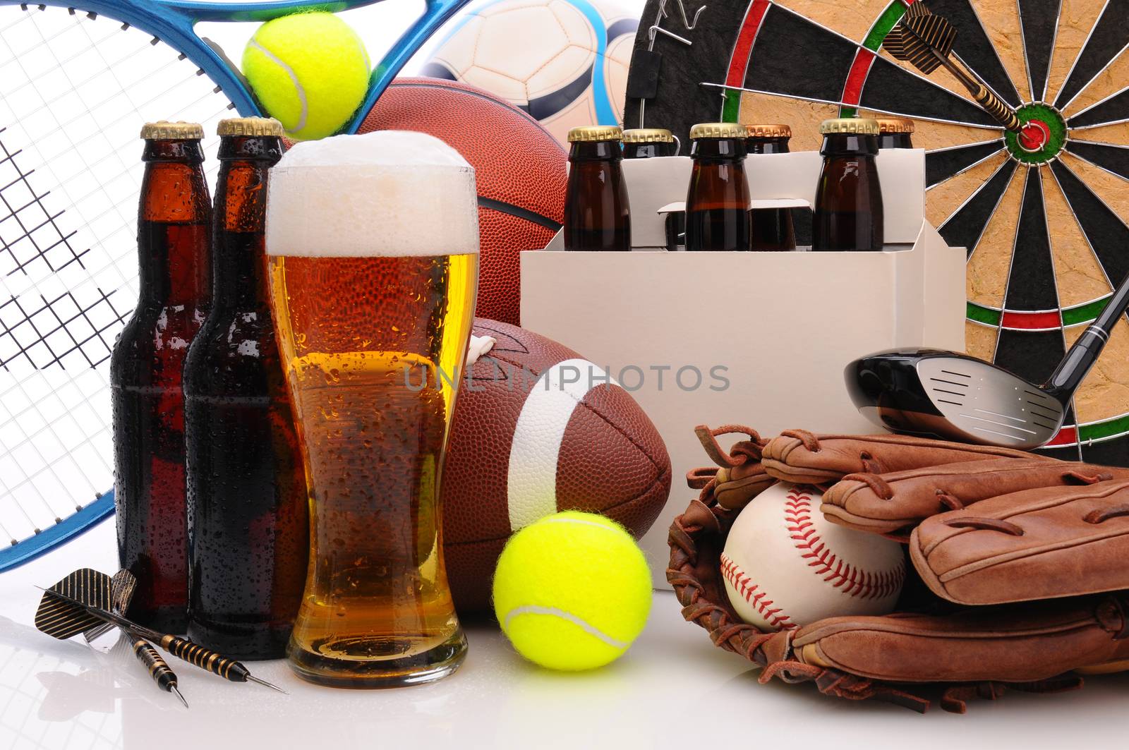Six pack of beer and frothy glass surrounded by sports equipment. Horizontal Format Filling the frame. Sports represented include, football, basketball, soccer, darts, baseball, tennis and golf.