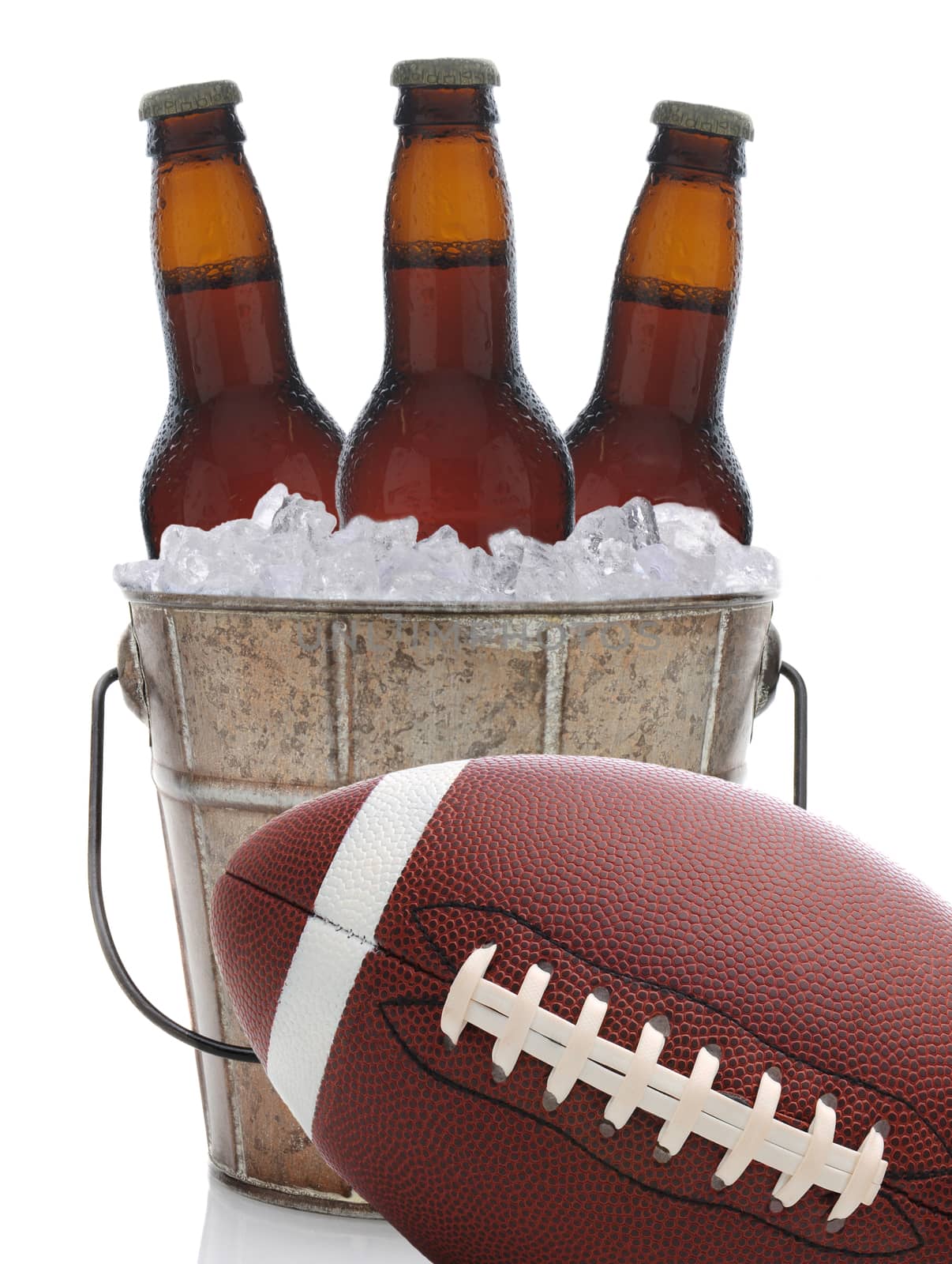 An old metal bucket with three brown beer bottles covered in condensation on a white background. An American football at an angle sits in front of the pail.
