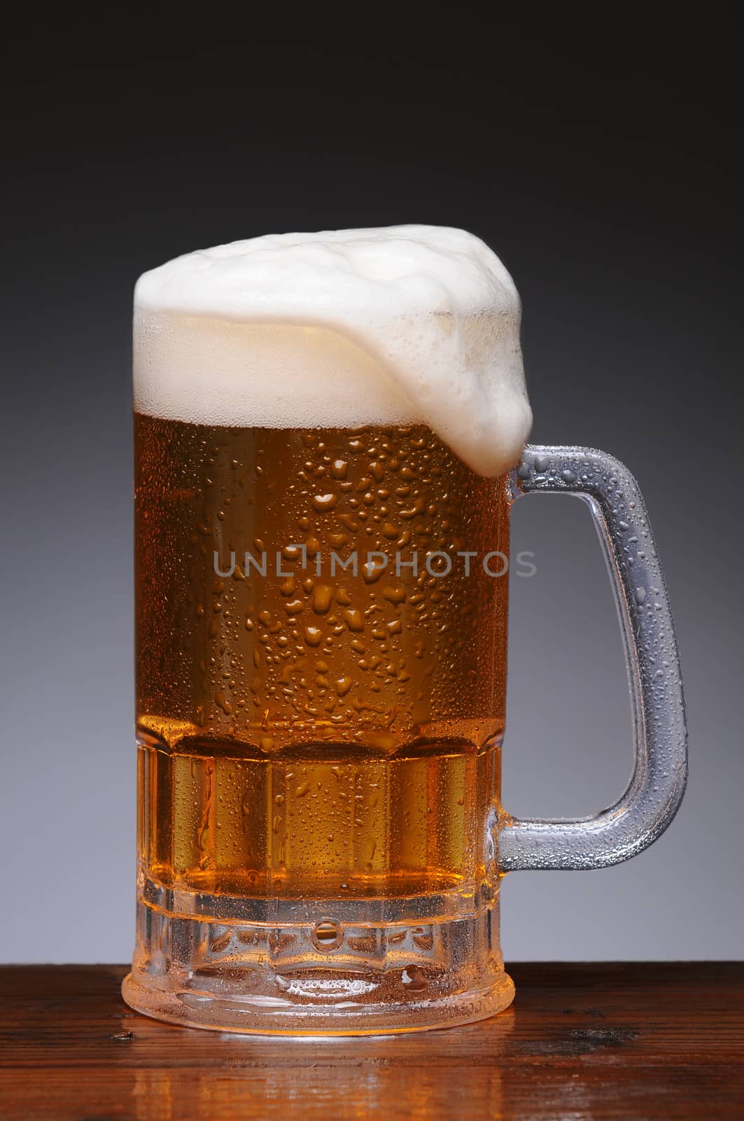 Closeup of a Frosty cold beer mug on a wet bar counter top. Vertical format with a light to dark gray background.