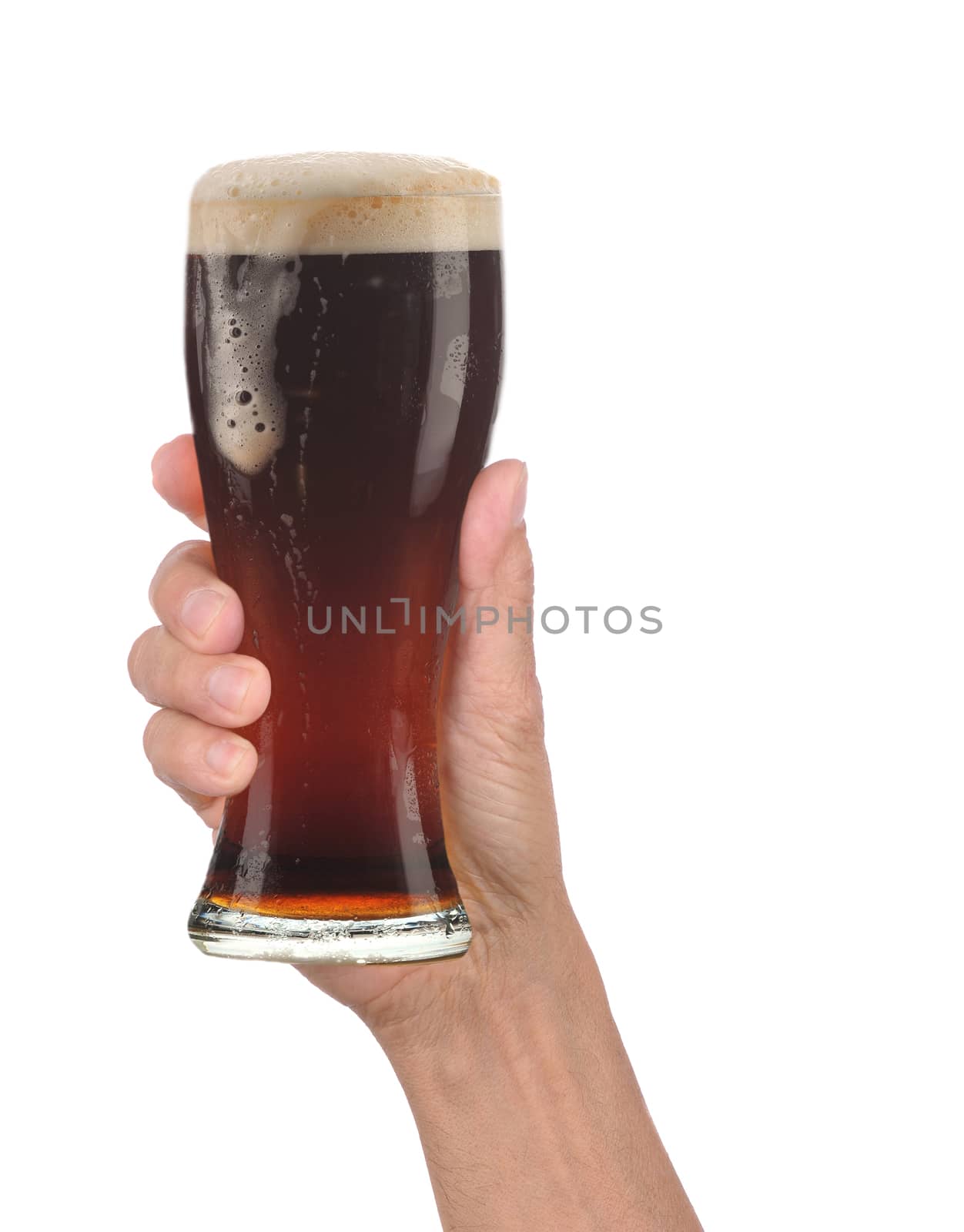 Closeup of a male hand holding up a glass of foamy dark ale over a white background. Vertical format with drip running down the side of the beer glass.