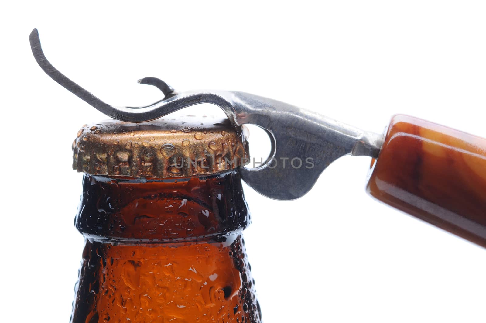 Macro shot of a brown beer bottle with an opener ready to pry up the bottle cap. Horizontal format over white.