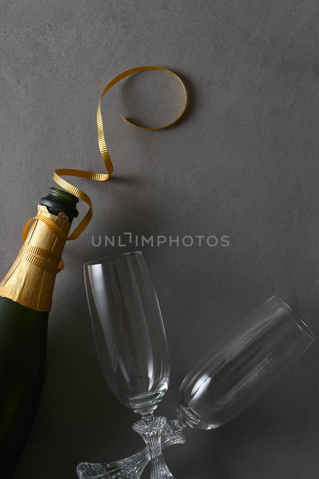 Champagne bottle with god ribbon and two glasses on a gray table.