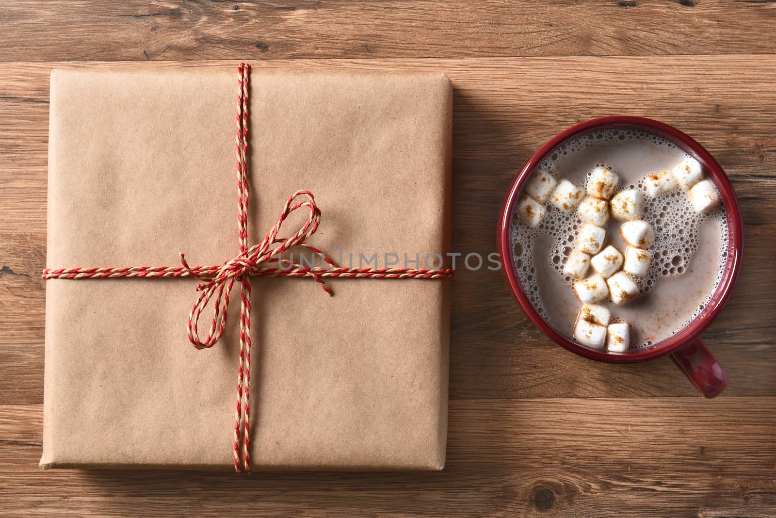 High angle view of a plain brown paper wrapped Christmas Present next to a large mug of hot cocoa with marshmallows.